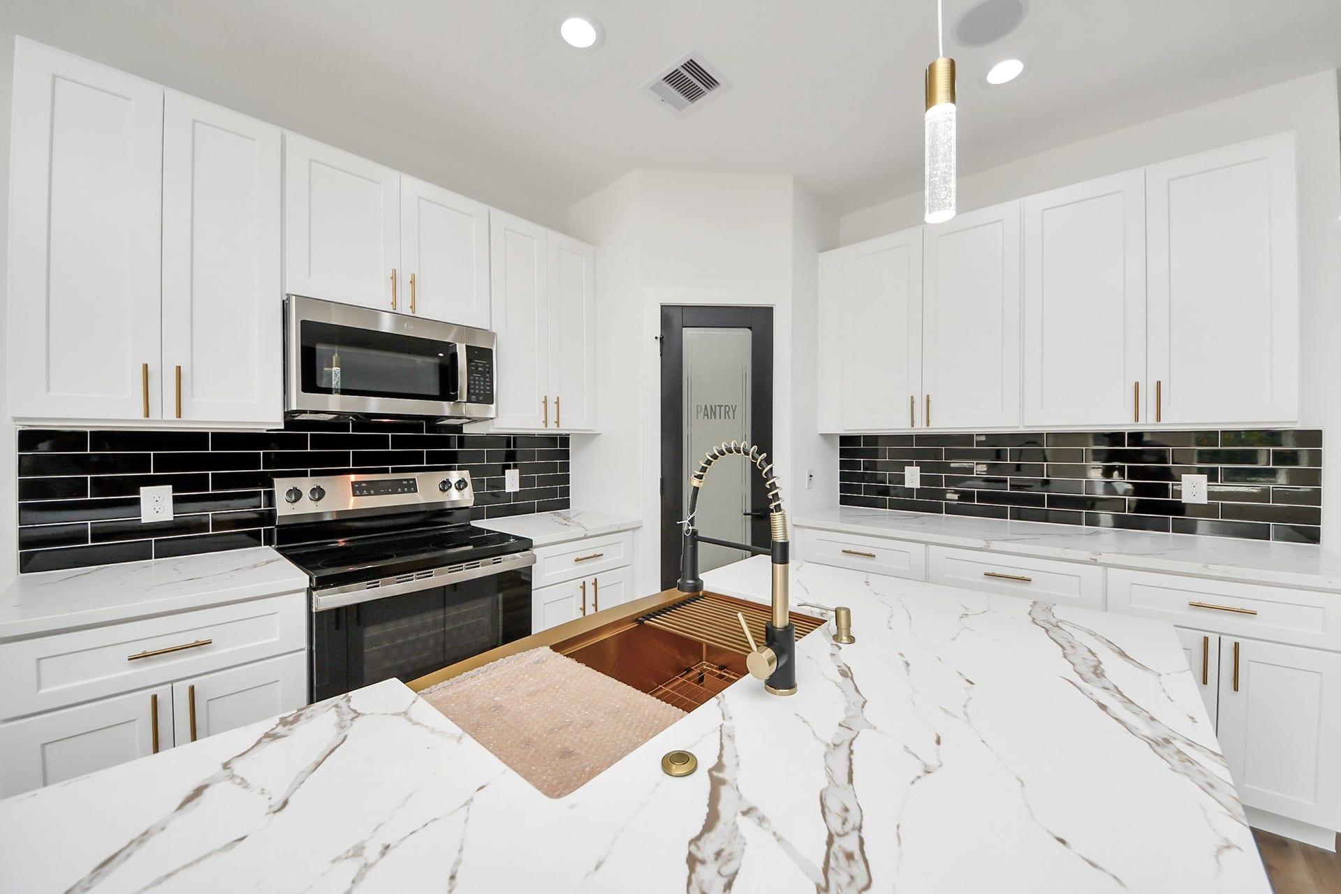 7801 King Street, Houston, TX 77028 Sleek and modern kitchen featuring elegant white cabinetry, striking black subway tile backsplash, and luxurious marble countertops, complete with a high-end stainless steel appliance suite.