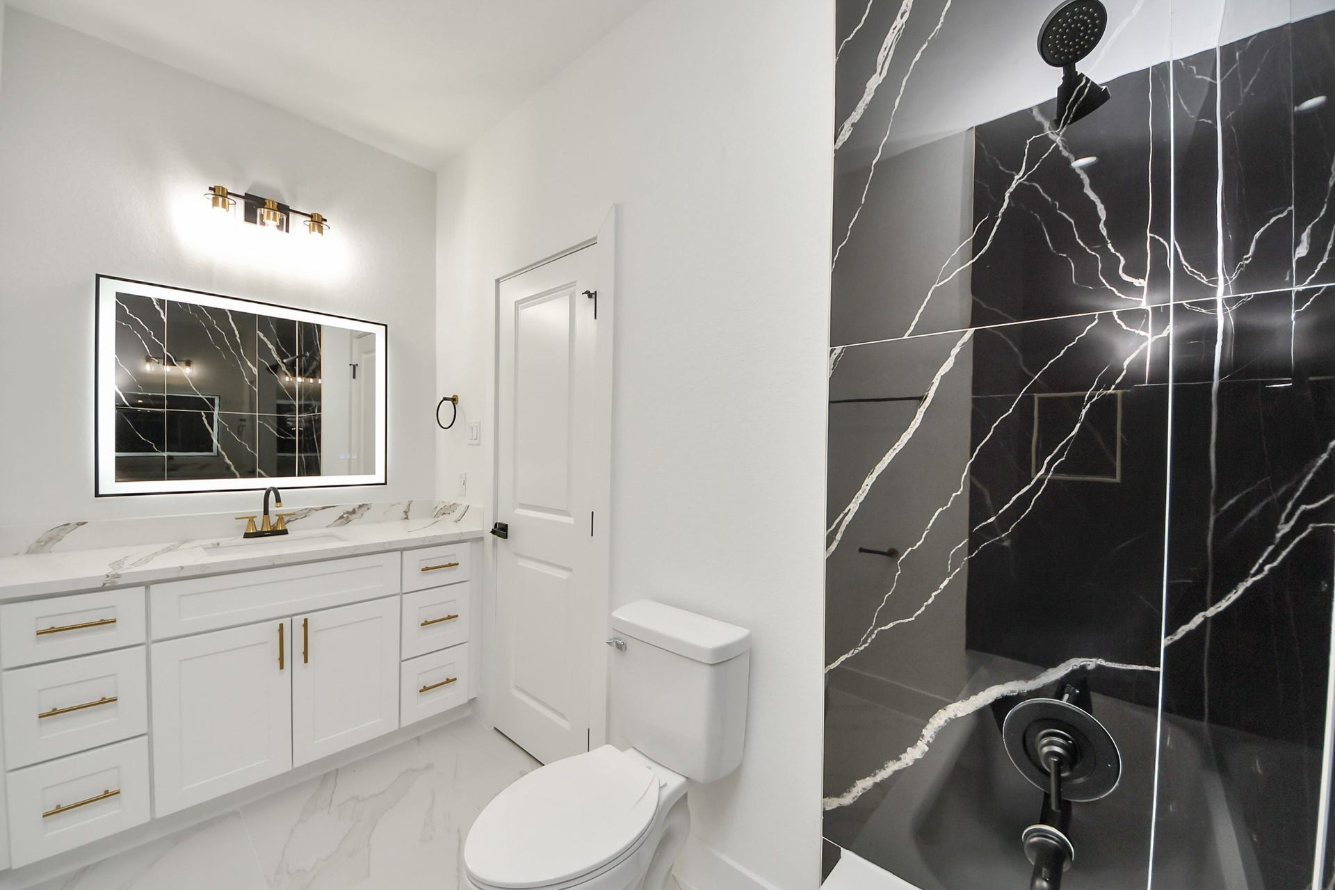 7801 King Street, Houston, TX 77028 Elegant bathroom featuring a striking black marble shower with white veining, complemented by a sleek vanity with gold fixtures and ample storage.