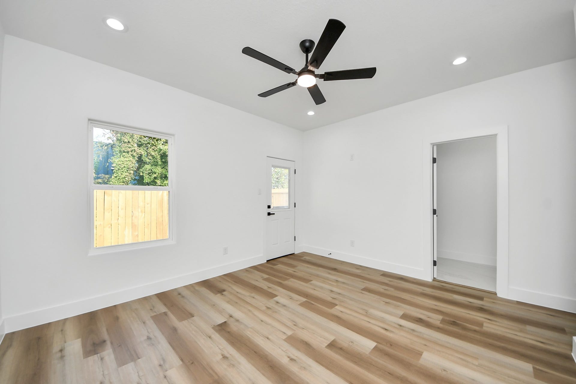 7801 King Street, Houston, TX 77028 Bright and airy room featuring sleek hardwood floors, recessed lighting, and a modern ceiling fan, with a window and door leading outside for easy access.