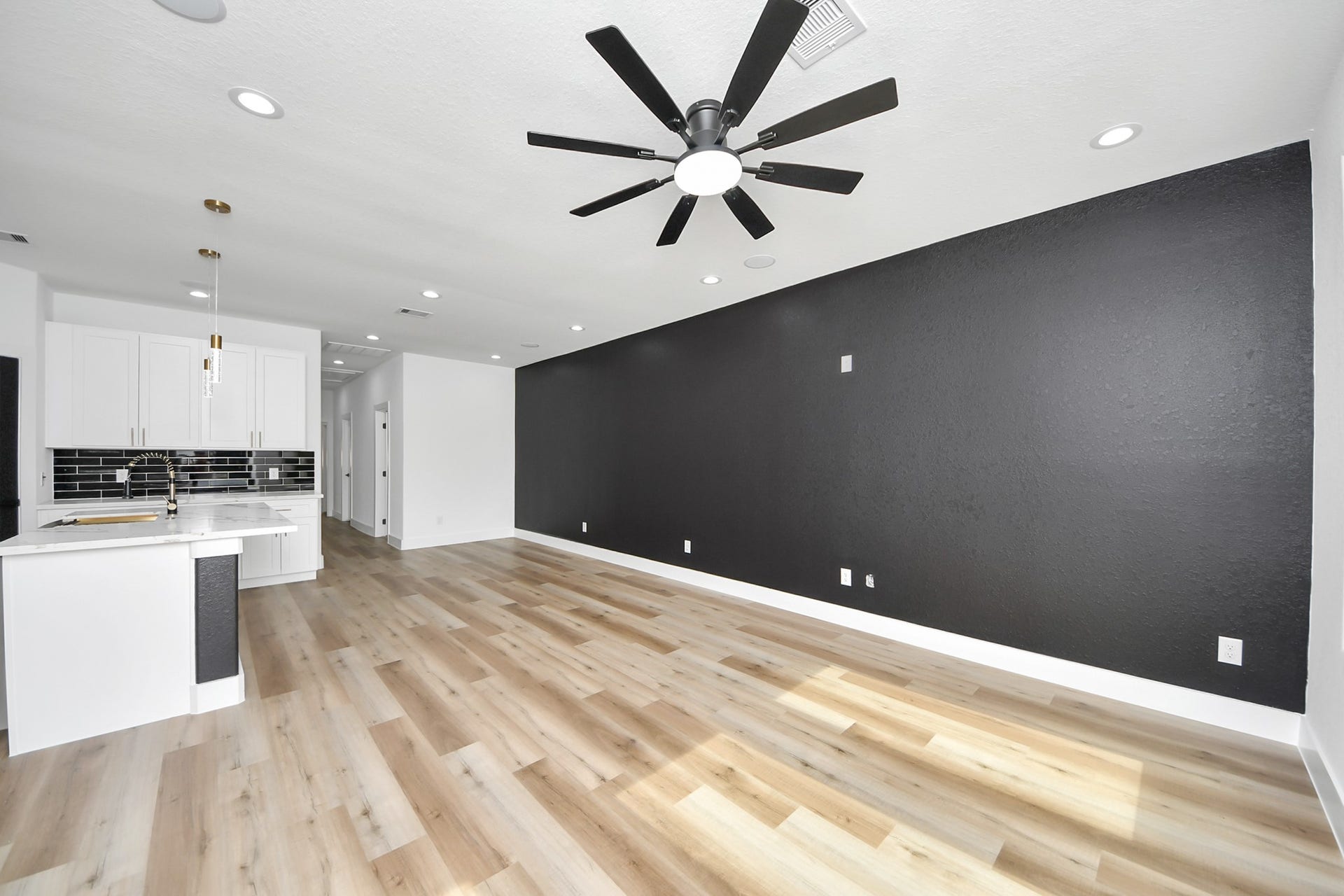 7801 King Street, Houston, TX 77028 Spacious open-concept living area features sleek wood flooring and a striking black accent wall, seamlessly flowing into a modern kitchen with chic black-and-white cabinetry and stylish backsplash.