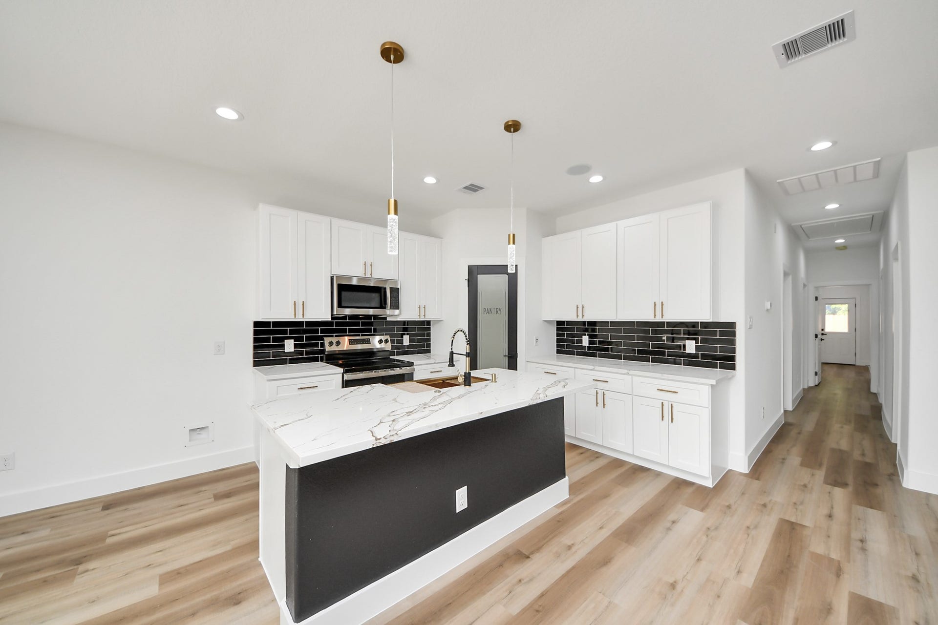 7801 King Street, Houston, TX 77028 Sleek modern kitchen featuring a spacious island with a marble countertop, elegant black backsplash, and stainless steel appliances, complemented by warm wood flooring.