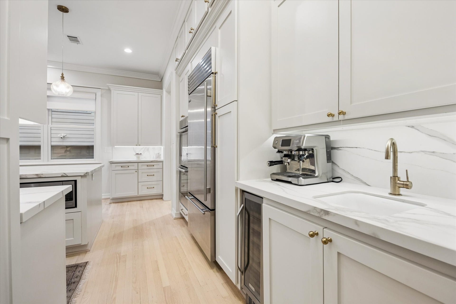 Thoughtfully designed beverage station features a prep sink, beverage refrigerator, stone countertop and dedicated space for a coffee baradding convenience and functionality to the kitchen.
