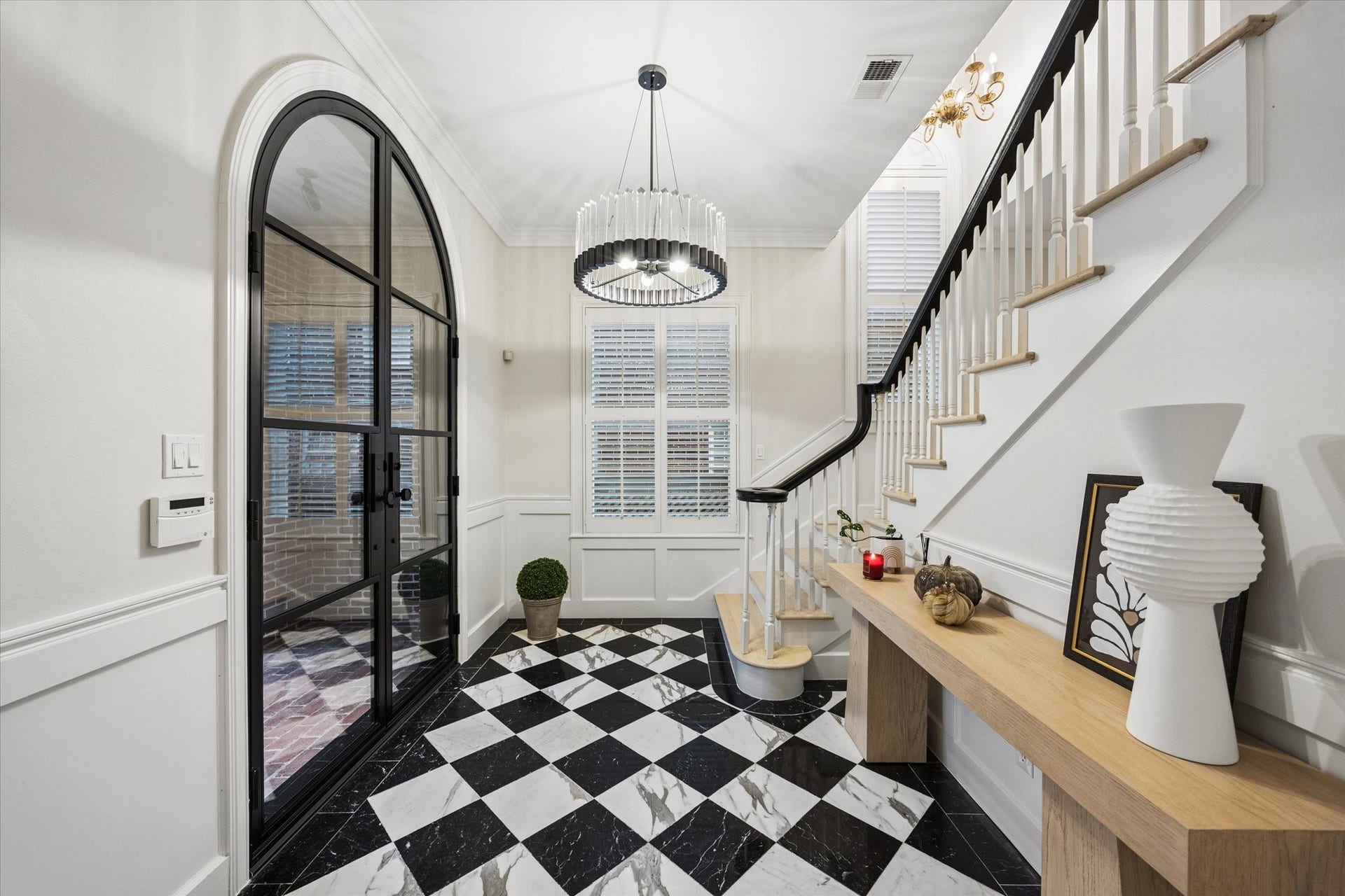 A refined view of the foyer showcases the striking black-and-white marble floors, graceful staircase, custom arched iron-and-glass entry door and elegant architectural detailing.