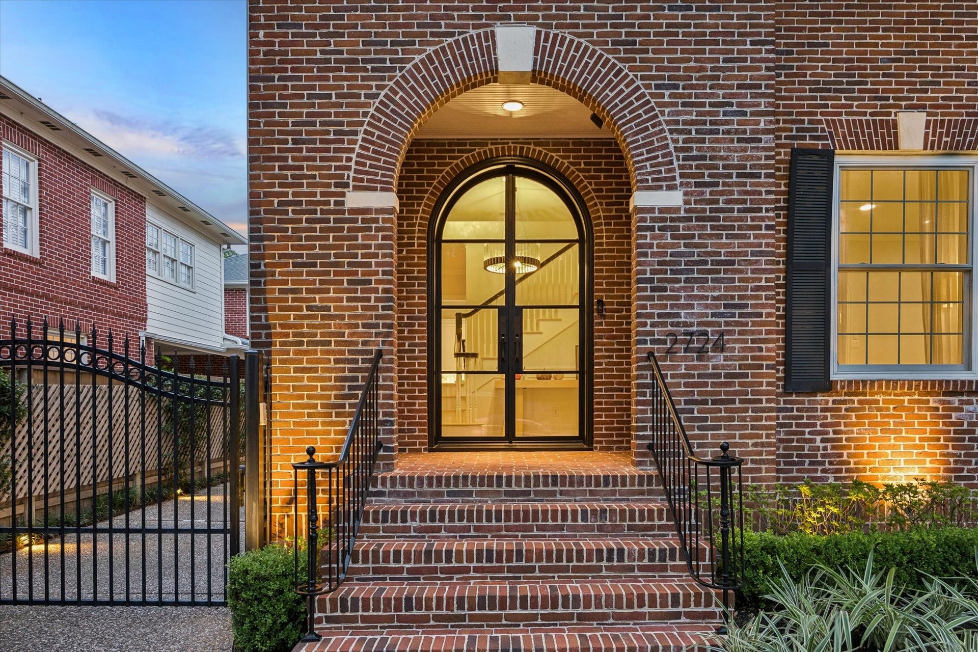 A striking arched entry with elegant brick detailing and a custom iron-and-glass front door creates a beautiful and inviting arrival.
