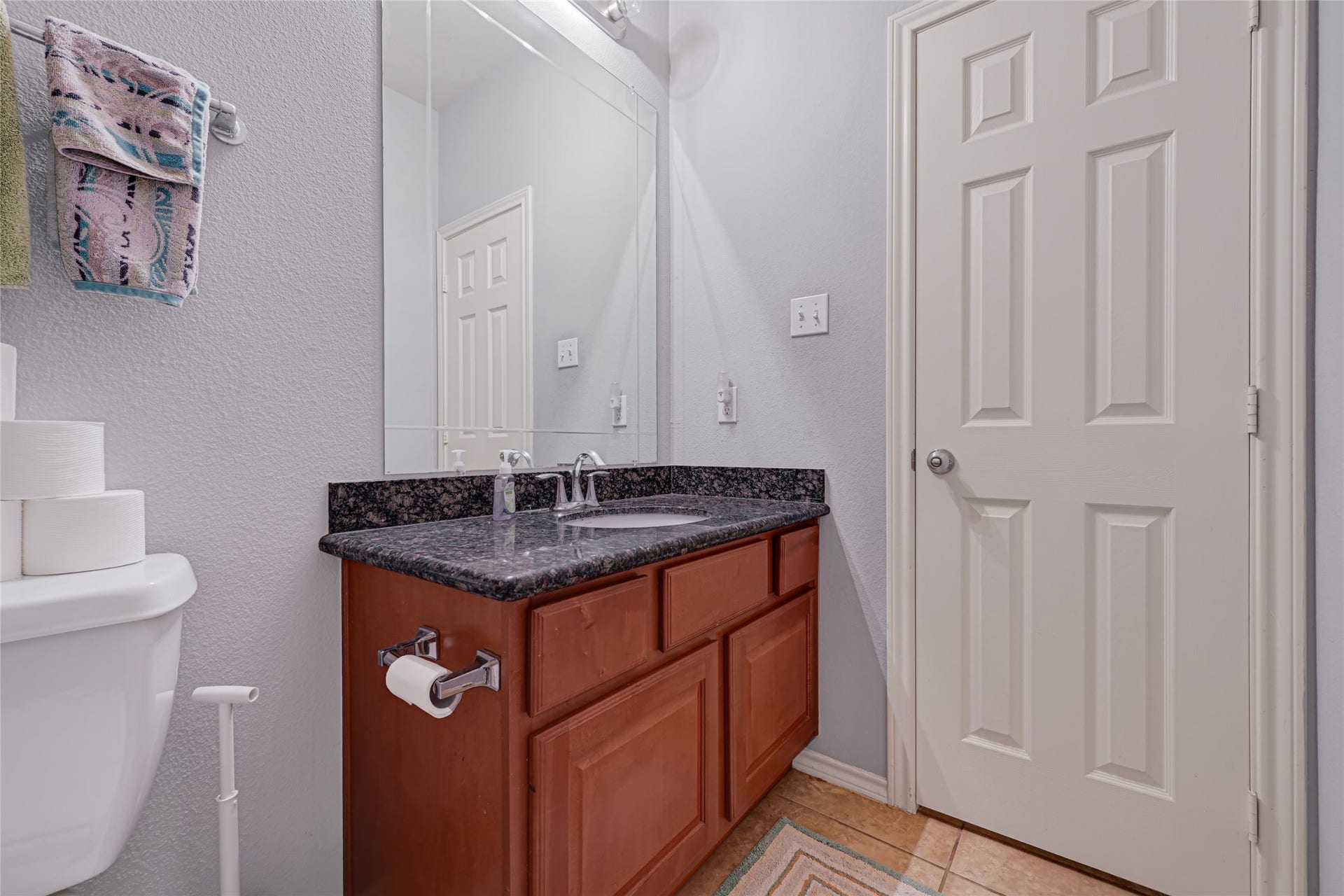 Charming bathroom featuring a sleek granite countertop, ample cabinet storage, and a large mirror, complemented by neutral tile flooring for a clean, modern look.