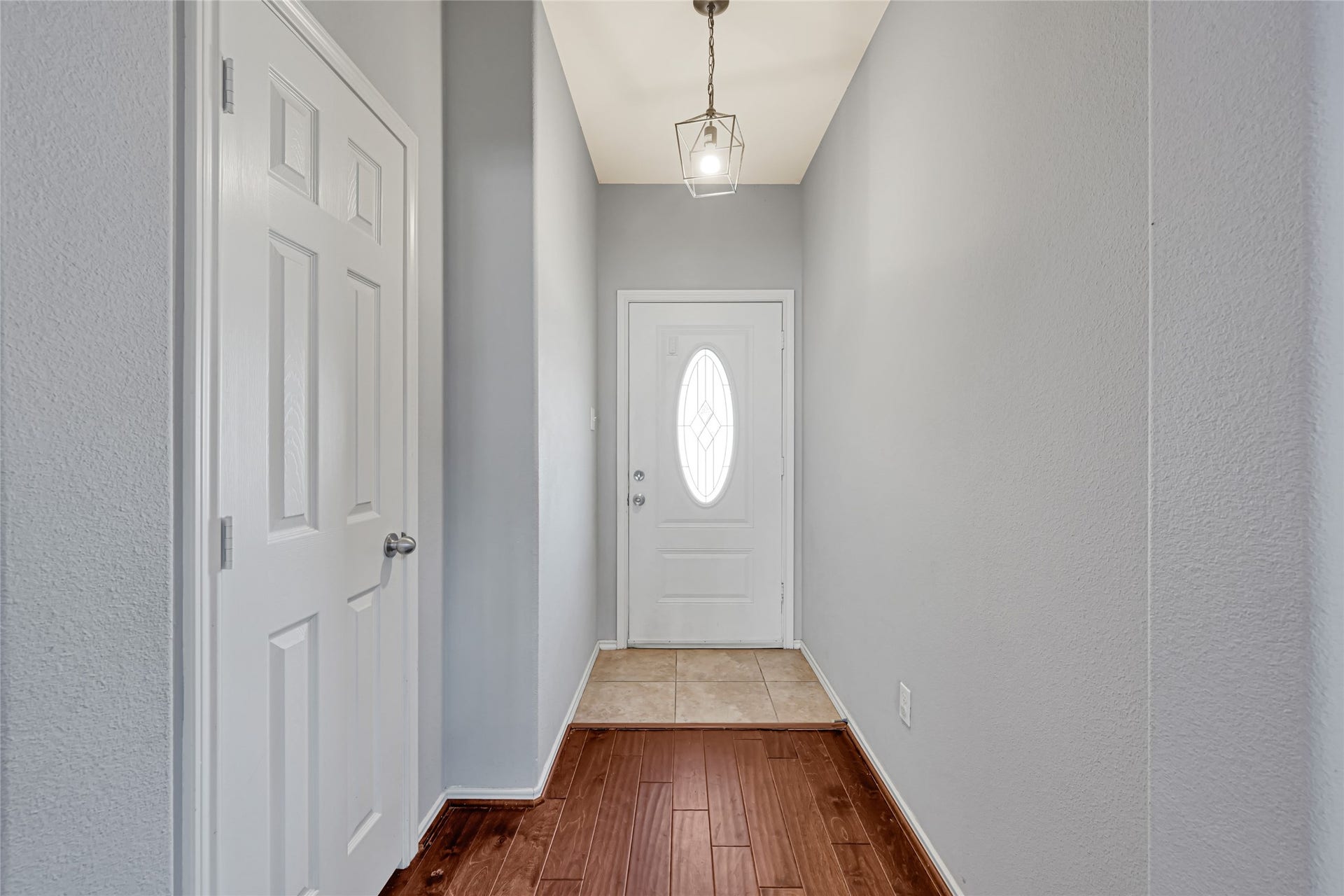 Inviting entryway with elegant wood and tile flooring, featuring a classic white door with decorative glass paneling and a modern pendant light.