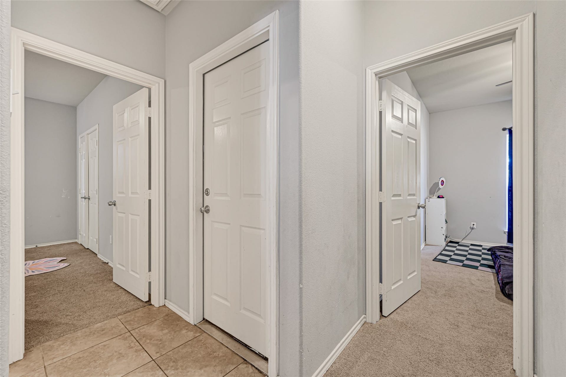 A welcoming hallway with neutral tones leads to multiple rooms, featuring a mix of carpet and tile flooring for a cozy and functional space.