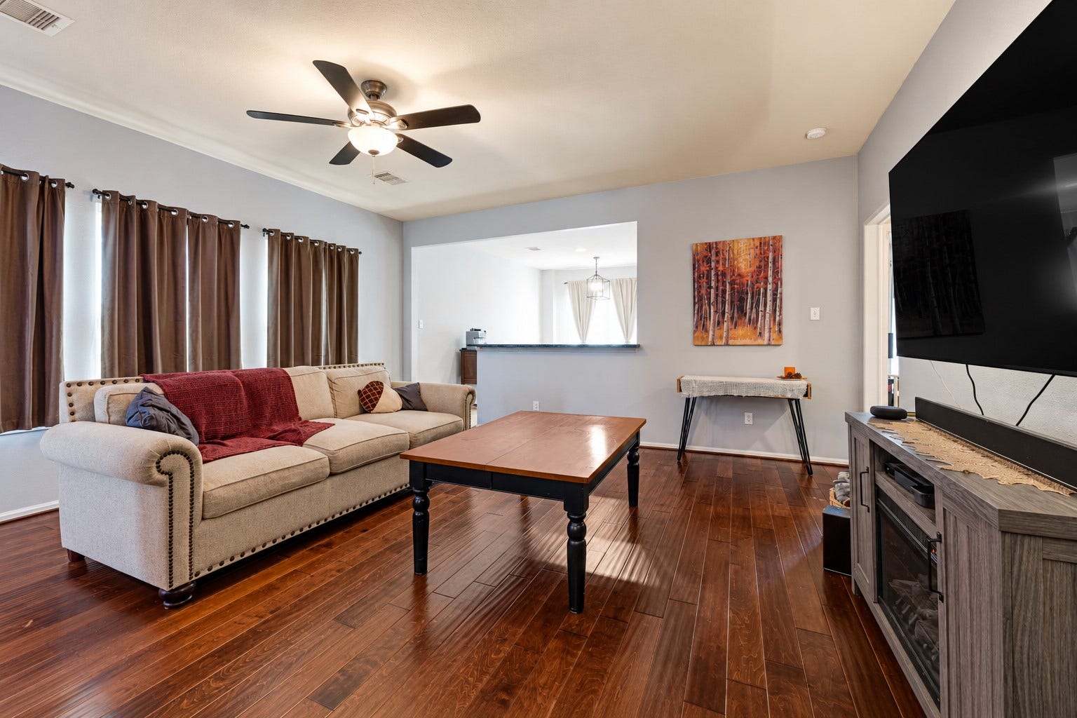Spacious living area with elegant hardwood floors, a cozy sectional sofa, and a modern ceiling fan, perfect for relaxation and entertainment.