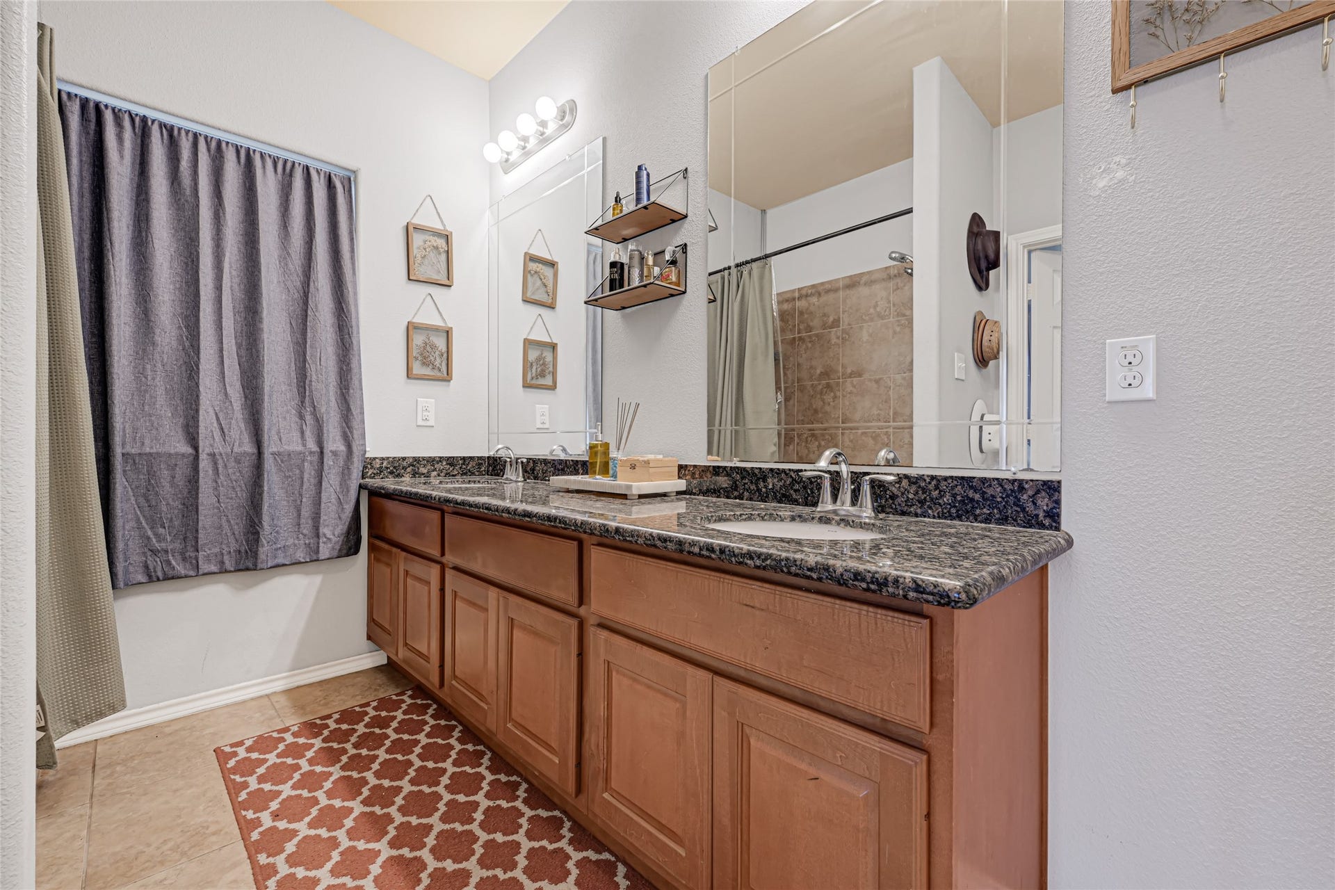 Spacious bathroom featuring a double vanity with granite countertops and ample storage, complemented by stylish lighting and a large mirror for a modern touch.