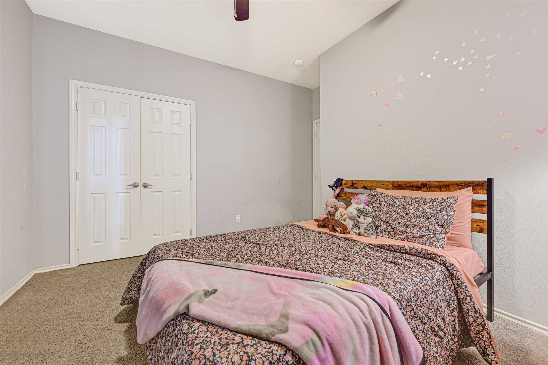 Cozy bedroom with soft carpeting, featuring a charming bed with floral bedding and decorative wall accents, perfect for a peaceful retreat.