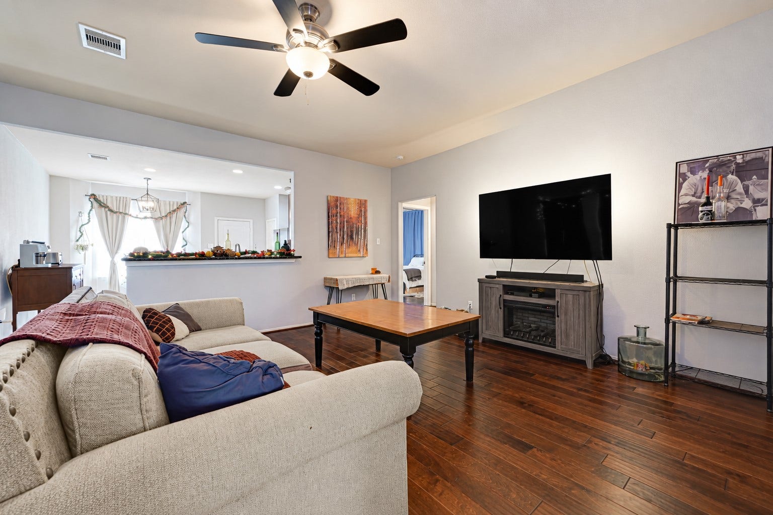Spacious living room with warm wooden floors, a cozy sectional sofa, and a large flat-screen TV, perfect for relaxation and entertainment.