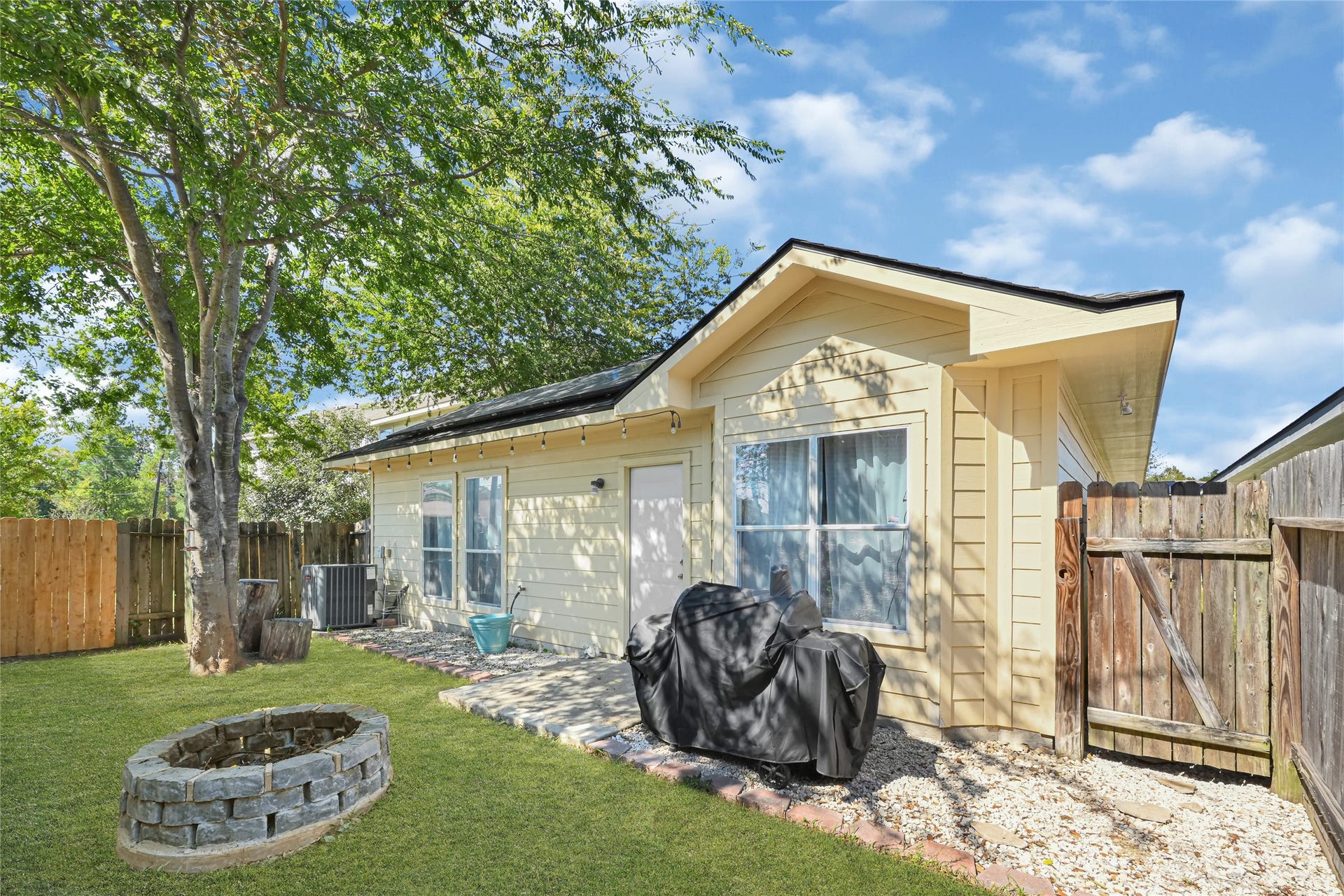 Charming backyard space featuring a cozy fire pit, mature tree, and a well-maintained exterior, perfect for outdoor gatherings.