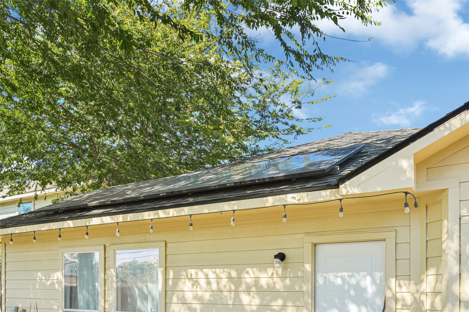 Charming home with energy-efficient solar panels and inviting outdoor lighting, nestled under the shade of mature trees.