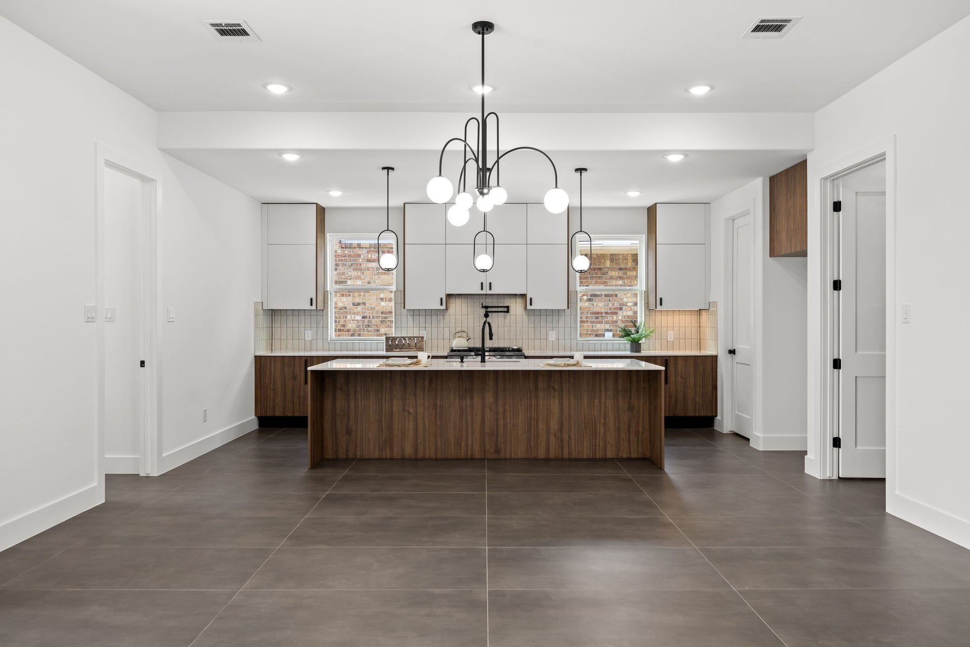 98 Camden Hills Drive, Montgomery, TX 77356 This photo showcases a modern kitchen with a large island featuring wood cabinetry and a sleek countertop. The room has white walls, contemporary pendant lighting, and tiled flooring. Ample cabinet space and a stylish backsplash complement the clean, open layout.