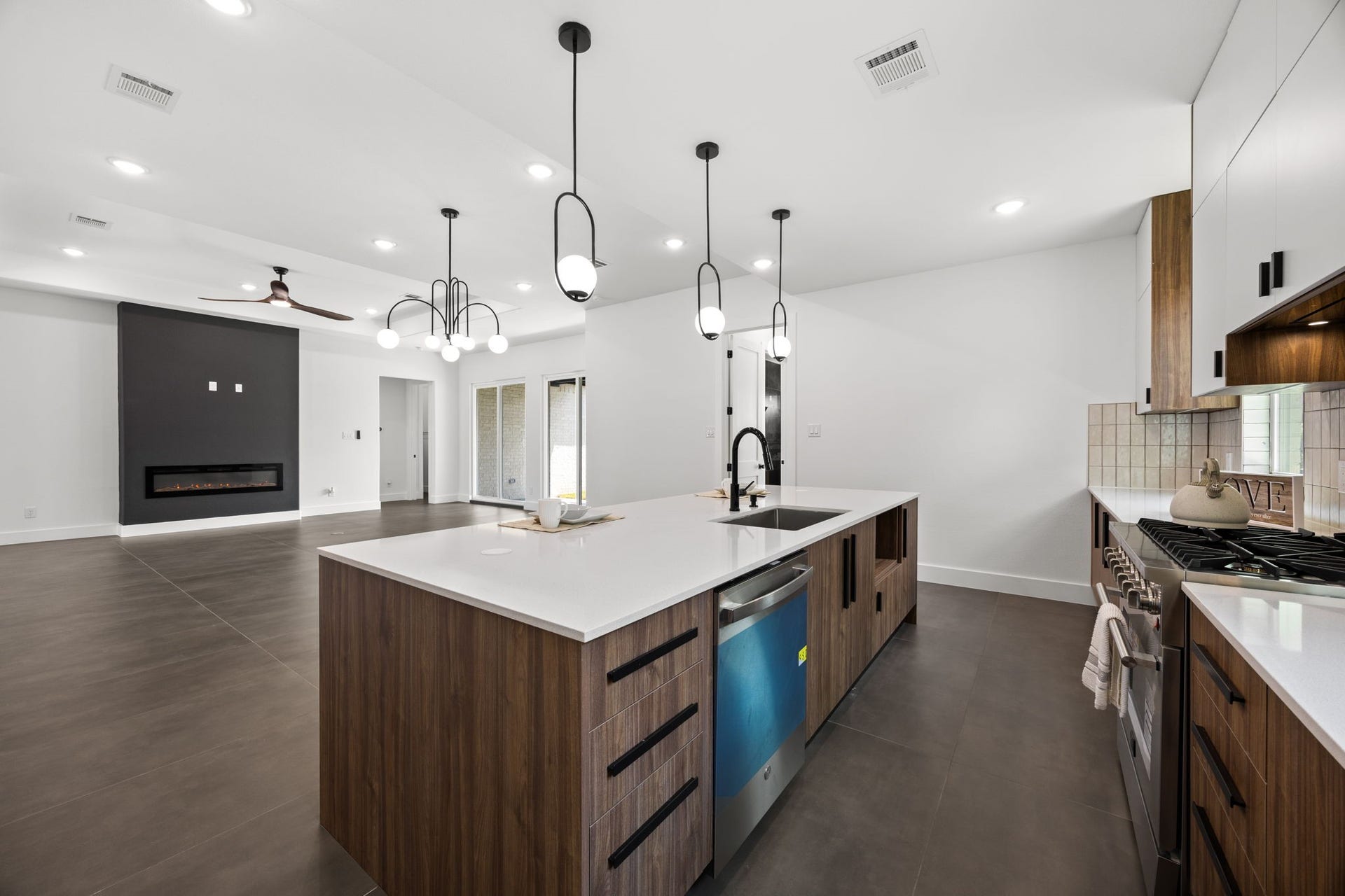 98 Camden Hills Drive, Montgomery, TX 77356 This modern kitchen and living area features an open layout with sleek finishes. The kitchen boasts a large island with pendant lighting, stainless steel appliances, and ample cabinetry. The living space includes a stylish fireplace and large windows for natural light.