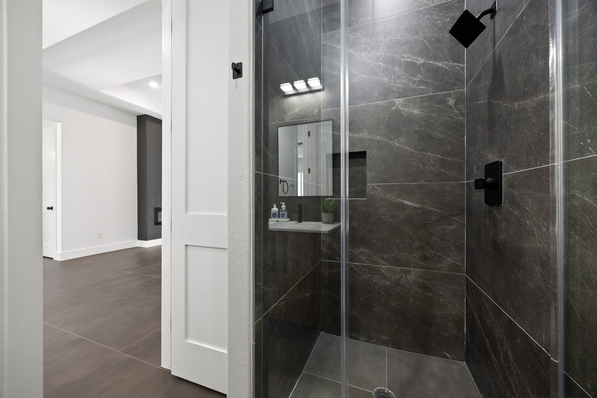 98 Camden Hills Drive, Montgomery, TX 77356 This photo showcases a modern shower with sleek, dark tiles and a glass enclosure. The adjacent room features a clean, minimalist design with large tiles and white walls, offering a contemporary aesthetic.