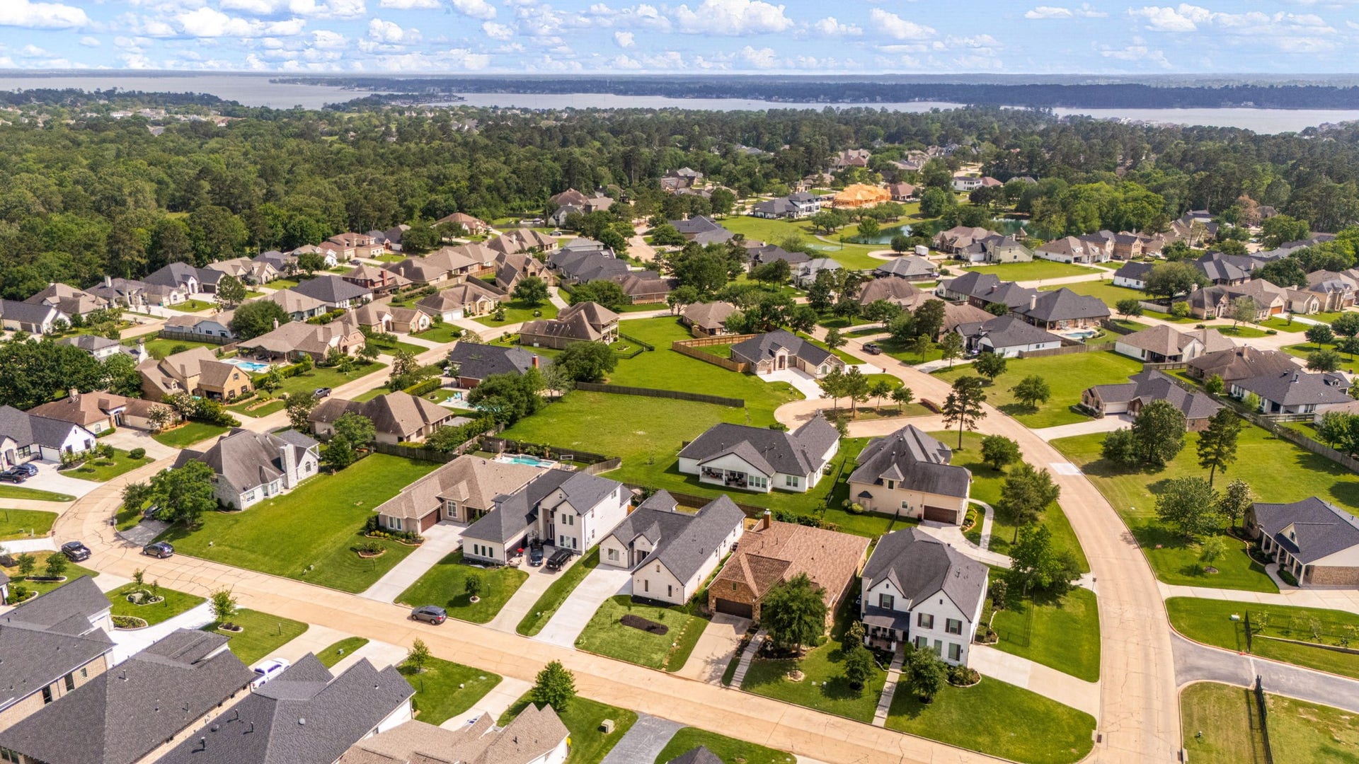 98 Camden Hills Drive, Montgomery, TX 77356 This aerial photo showcases a picturesque residential neighborhood with well-maintained homes, spacious yards, and tree-lined streets. The community is surrounded by lush greenery and is located near a large body of water, offering a serene and inviting environment.