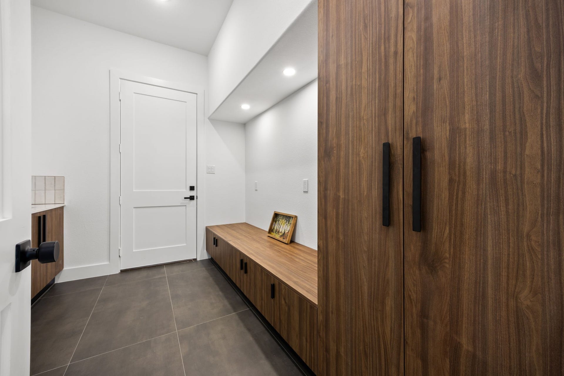 98 Camden Hills Drive, Montgomery, TX 77356 This photo showcases a modern mudroom with sleek, dark tile flooring, white walls, and stylish wood cabinetry. It features built-in storage with a bench, recessed lighting, and a clean, minimalist design.