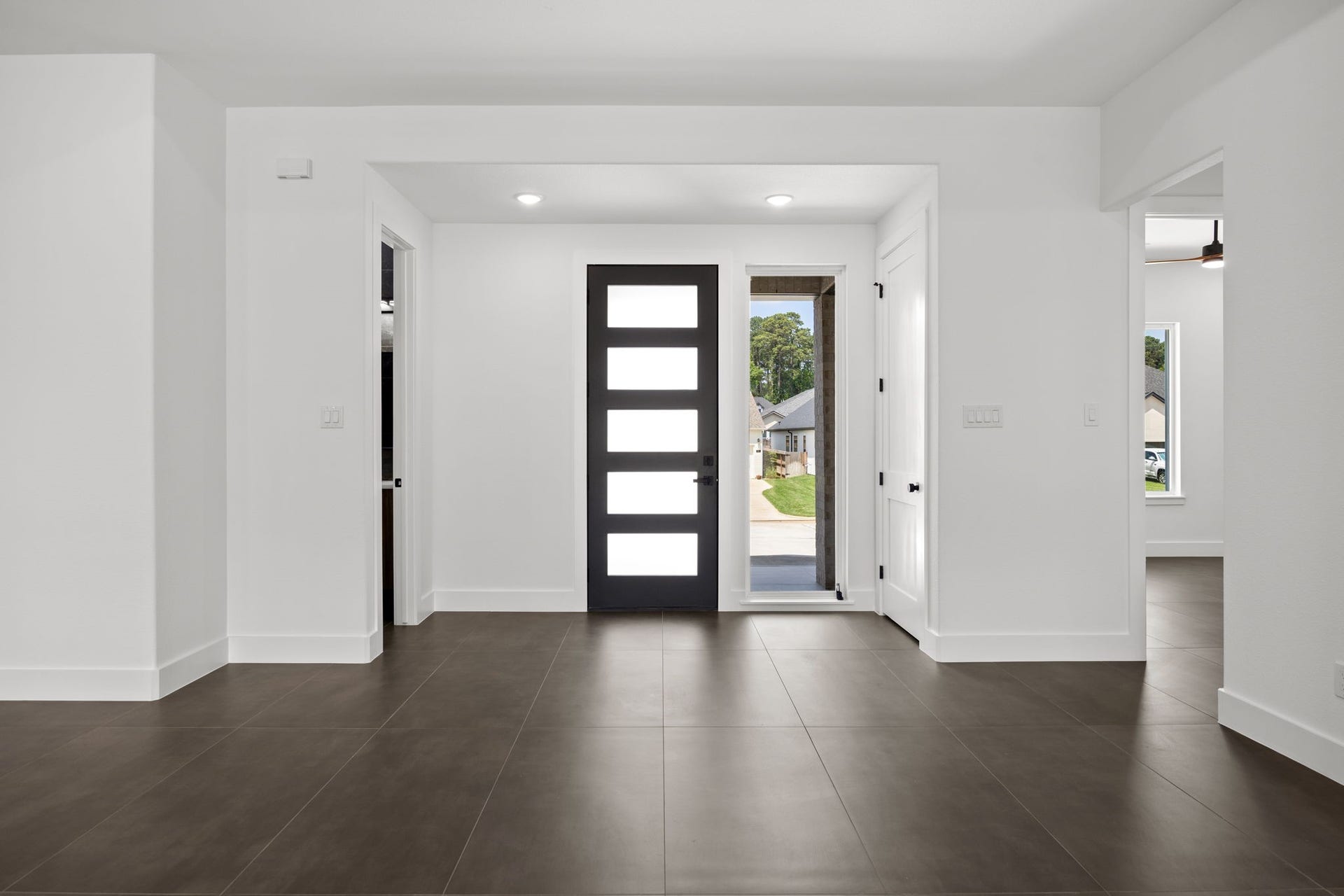 98 Camden Hills Drive, Montgomery, TX 77356 This photo shows a modern entryway with a sleek black door featuring horizontal glass panels. The space is bright and open, with large brown tiles and neutral white walls, creating a welcoming and contemporary atmosphere.