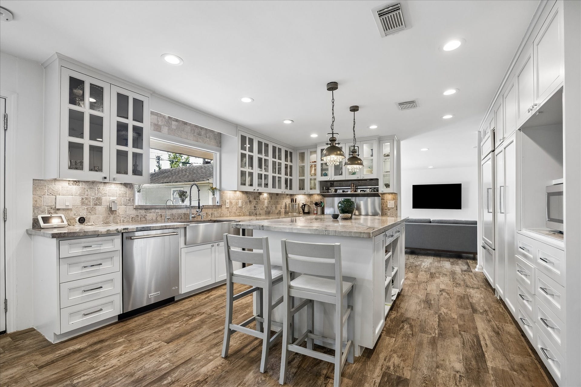 4703 Banning Drive, Houston, TX 77027 Beautifully updated kitchen features custom white cabinetry, glass-front upper cabinets, stone countertops, tile backsplash, stainless steel appliances & a large island w/breakfast bar seating. Decorative pendant lighting adds a distinctive touch.