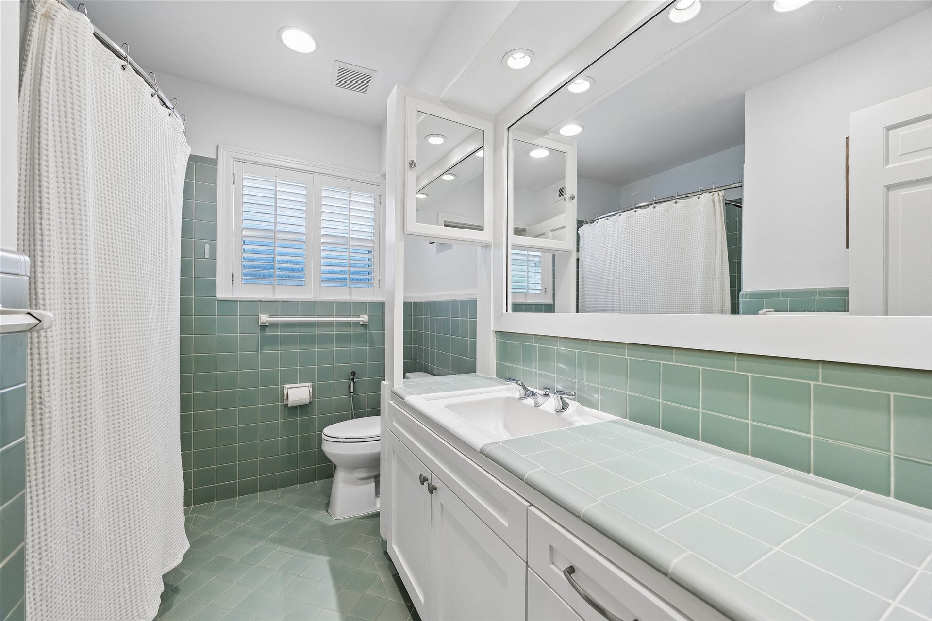4703 Banning Drive, Houston, TX 77027 Secondary bath features classic mint-green tile flooring, walls & countertop, white cabinetry w/storage, oversized vanity mirror, recessed lighting & tub/shower combination.