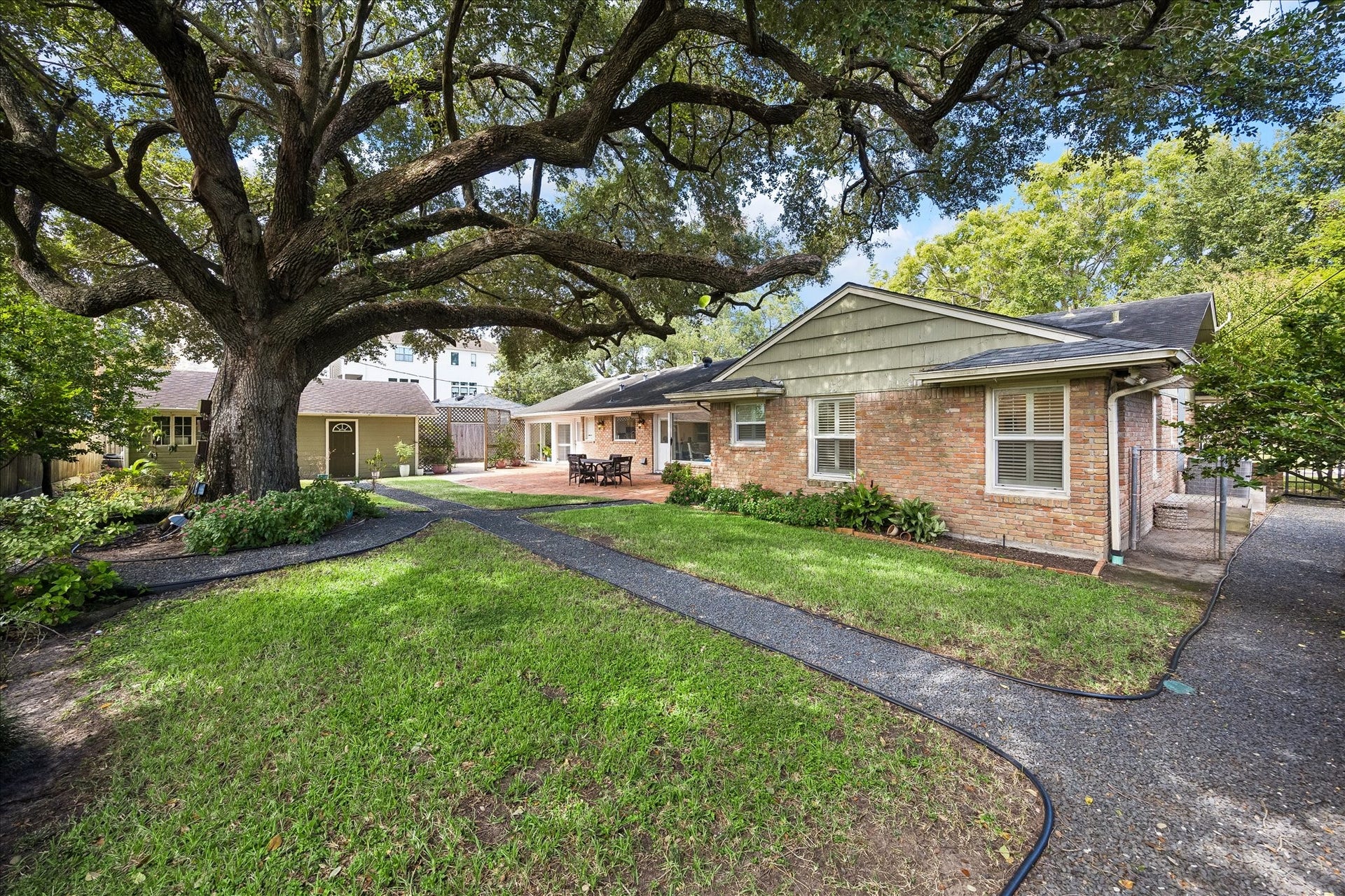 4703 Banning Drive, Houston, TX 77027 Rear exterior showcases the home's classic brick faade, expansive lawn & established landscaping. Winding pathways connect the outdoor spaces, while the detached 2-car garage offers convenient parking & additional storage possibilities.