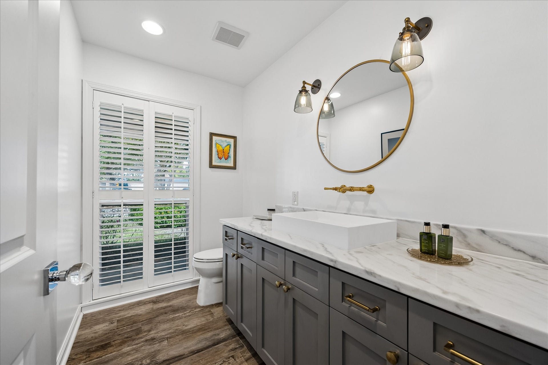4703 Banning Drive, Houston, TX 77027 Beautiful half bath features a sleek rectangular vessel sink, stone countertop, gray cabinetry w/brass hardware & a stylish round mirror. Decorative wall sconces, wall-mounted faucet, wood flooring & large window w/plantation shutters complete the space.