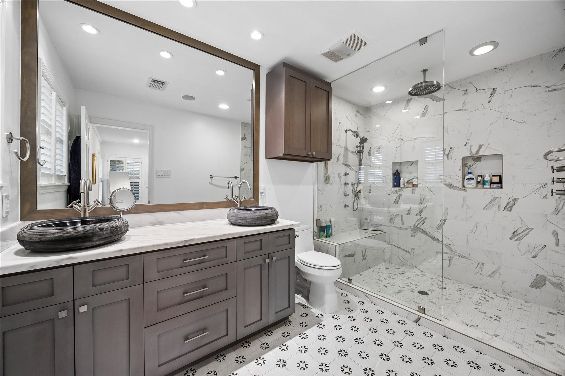 4703 Banning Drive, Houston, TX 77027 Beautifully updated primary bath features dual vessel sinks, stone countertop, custom cabinetry, oversized mirror & decorative tile flooring. Expansive glass-enclosed shower offers gorgeous tile, rainfall showerhead, handheld shower, built-in bench & recessed niches.