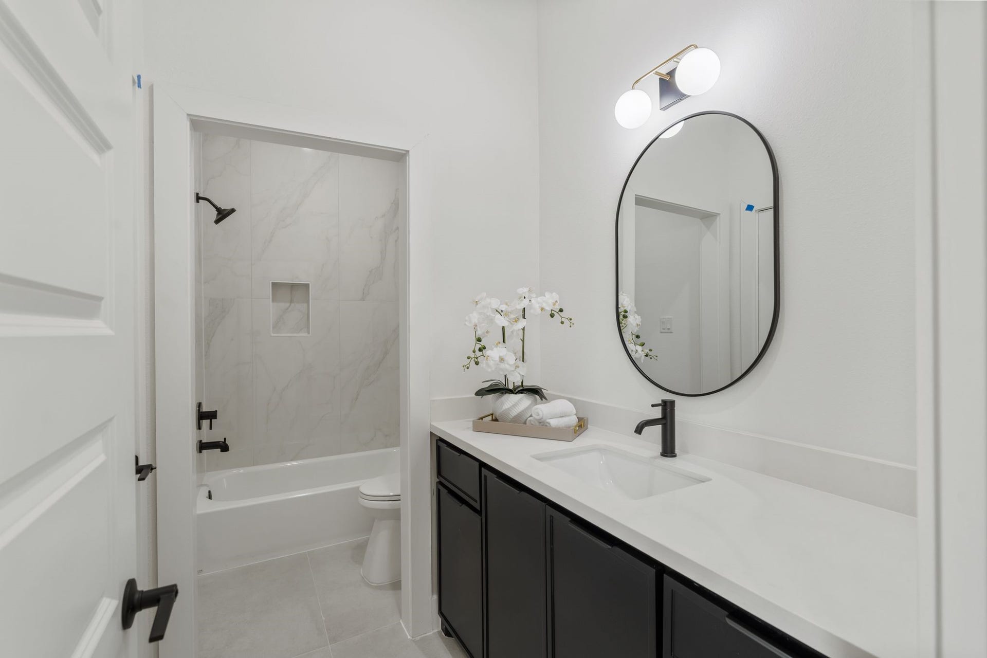Sleek bathroom with modern fixtures, featuring a tiled shower-tub combo and elegant vanity with an oval mirror.