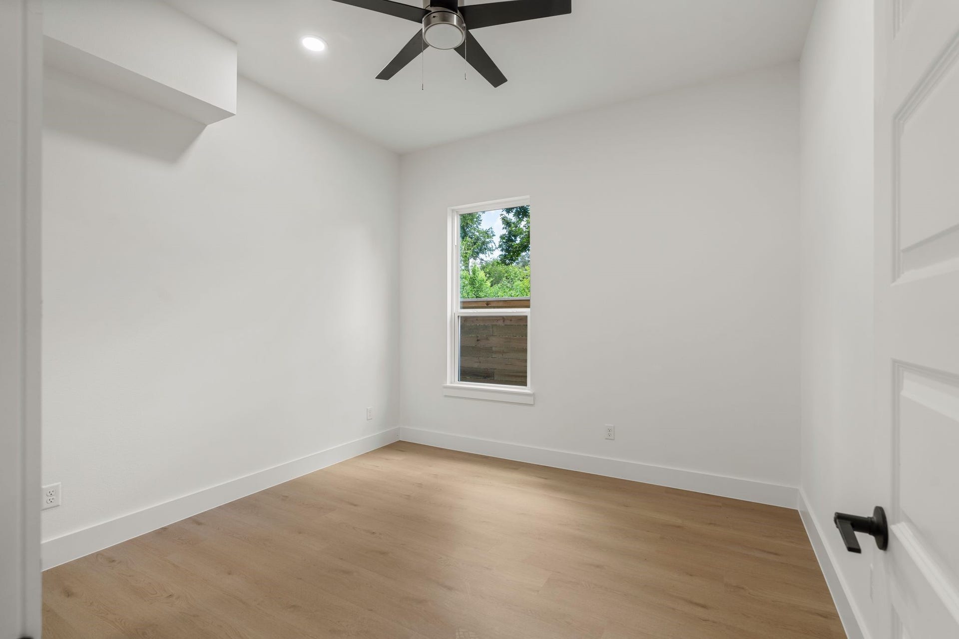 Bright and inviting room with sleek hardwood floors, crisp white walls, and a modern ceiling fan, perfect for a cozy retreat.