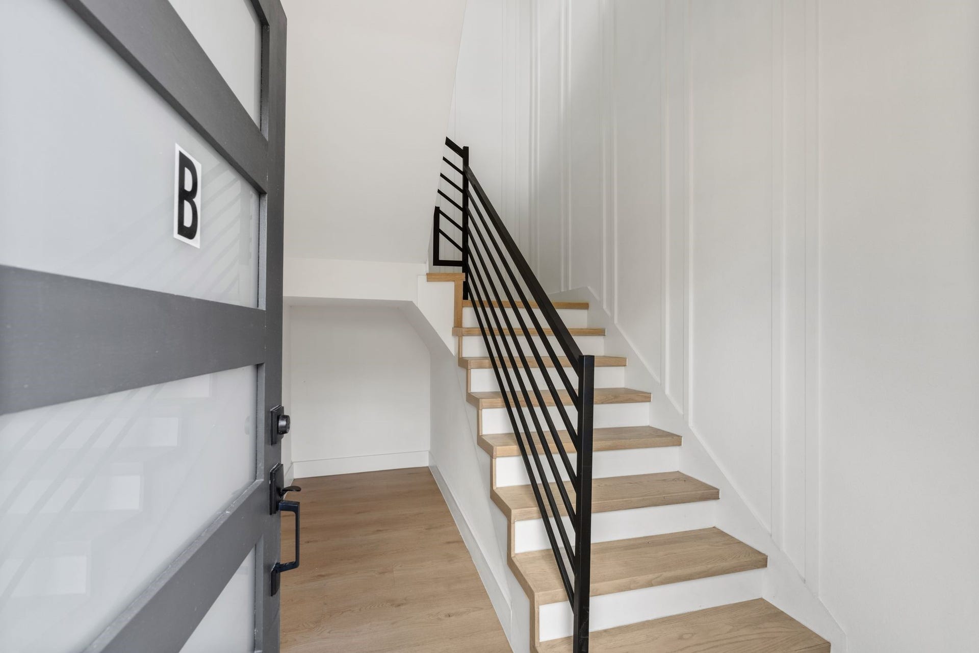 Contemporary entry way featuring sleek wooden stairs with modern black railings and minimalist white walls, creating a clean and inviting first impression.
