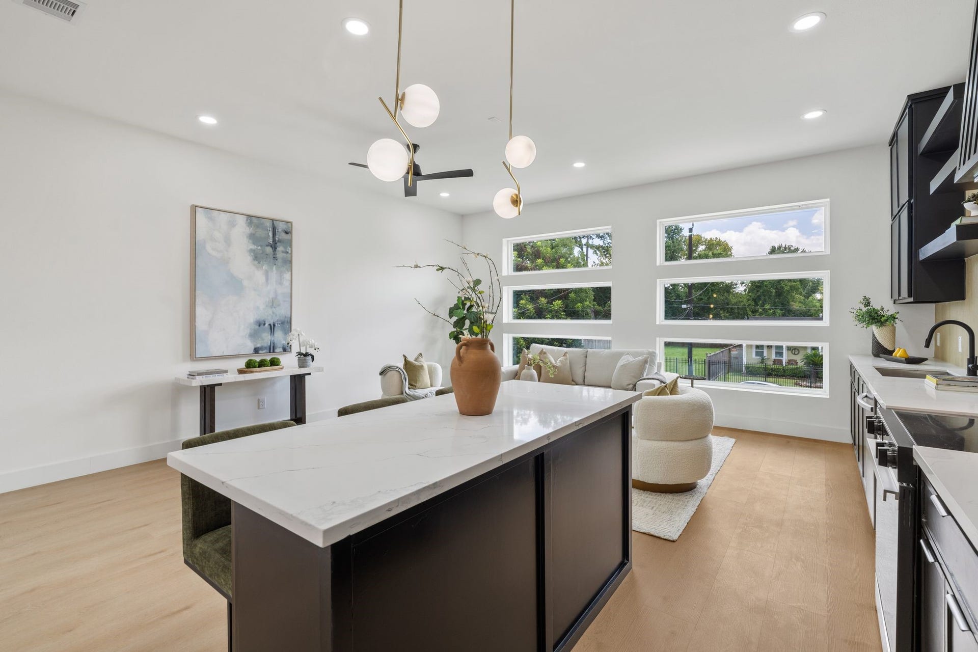 Experience modern elegance in this open-concept kitchen and living area, featuring sleek black cabinetry, a spacious island, and abundant natural light from large windows.