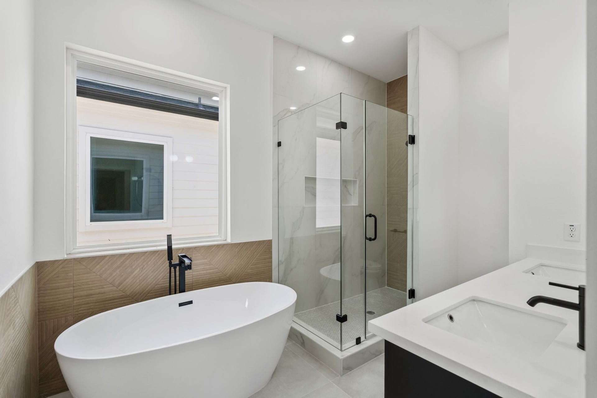 Sleek and modern bathroom featuring a free standing tub, walk-in glass shower, and dual sinks with elegant black fixtures.