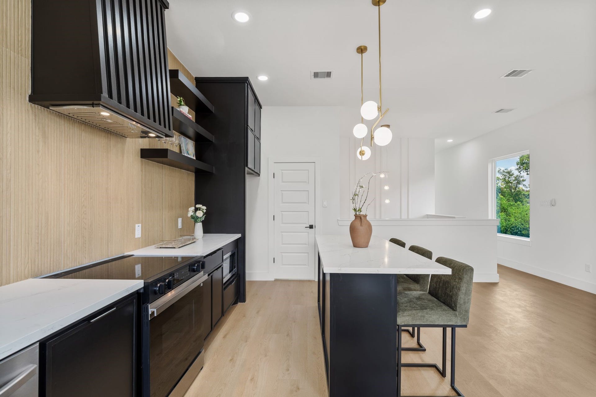 Sleek modern kitchen with black cabinetry, elegant pendant lighting, and a spacious island with seating, all set against warm wood flooring and a bright, open layout.