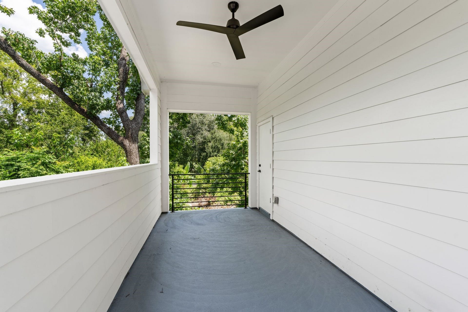 Spacious covered balcony with a ceiling fan, offering serene views of lush greenery.