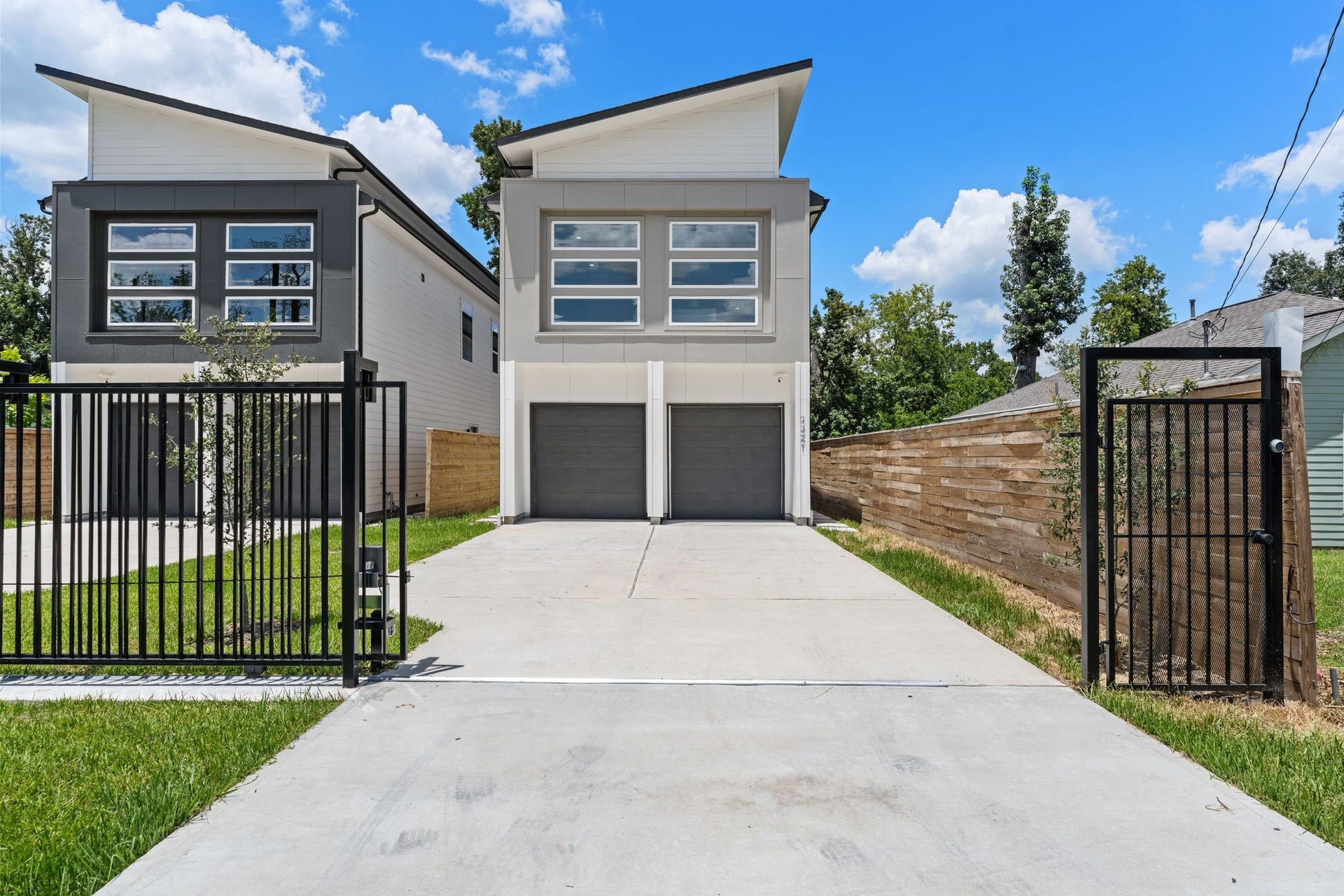 Modern new construction luxury duplexes with sleek lines and large windows are set behind a secure black iron gate, featuring a long shared driveway and well and private garages.