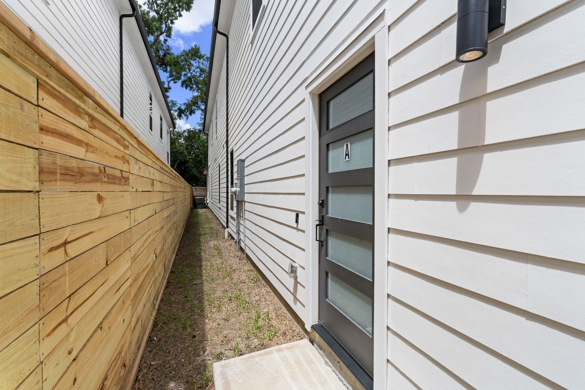 Modern side entrance with sleek panel door, bordered by a wooden privacy fence, offering a clean and private entryway