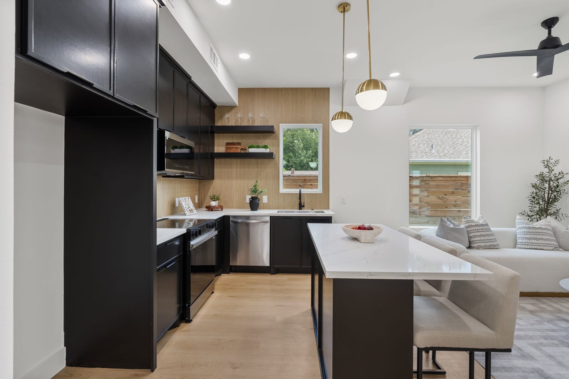 Sleek, modern kitchen with black cabinetry, acentral island, and elegant pendant lighting, seamlessly connected to a cozy living area.