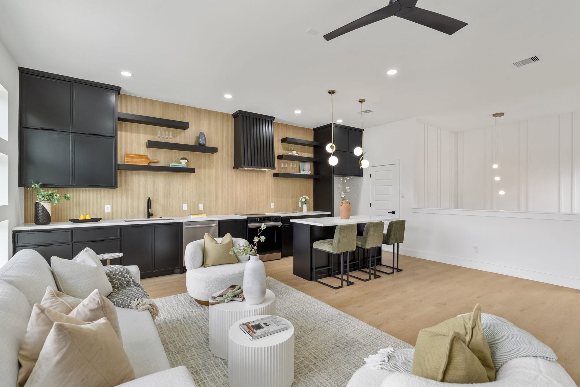 Sleek open-concept living area with a modern kitchen featuring black cabinetry, open shelving, and a spacious island with seating. Cozy lounge space offers comfort and style, perfect for entertaining.