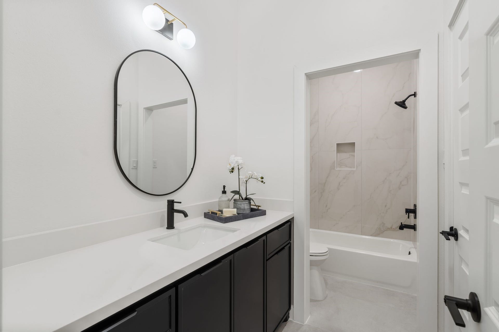 Sleek modern bathroom featuring a chic black vanity with dual sinks, an elegant oval mirror, and a bathtub with stylish marble-look tile