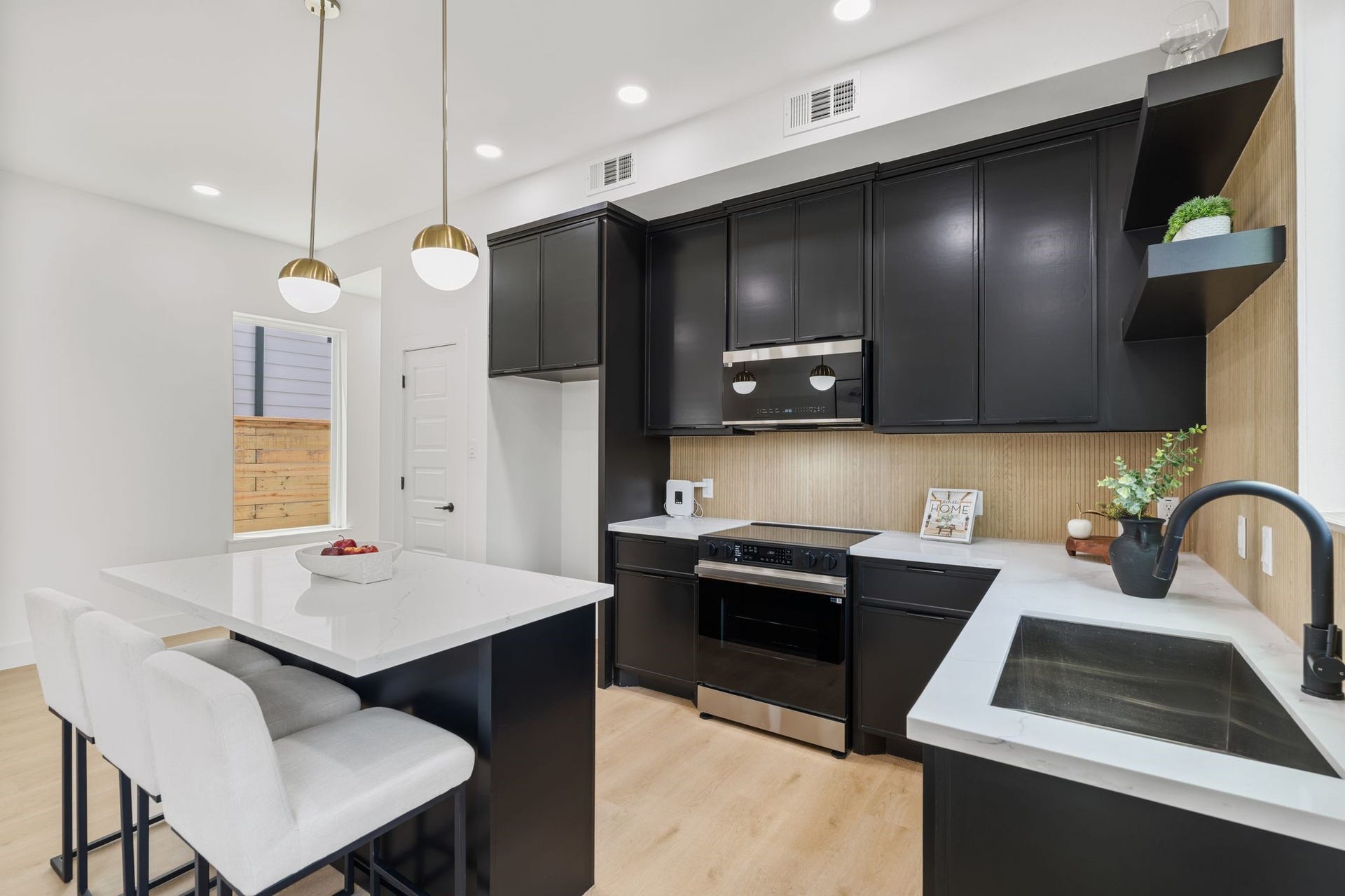 Sleek modern kitchen featuring black cabinetry, stainless steel appliances, and a spacious quartz island with seating. Elegant pendant lighting adds a touch of sophistication.