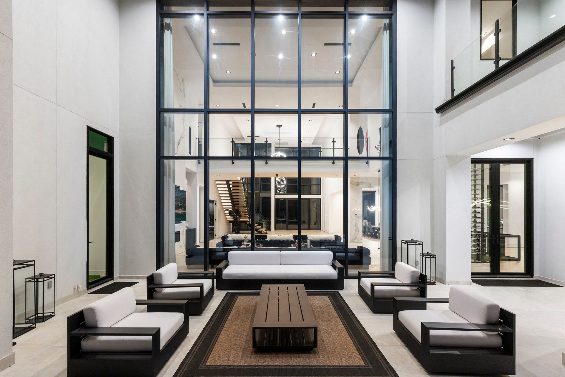 A two-story glass curtain wall seamlessly connects the main interior living room to an exquisite, covered outdoor atrium lounge.