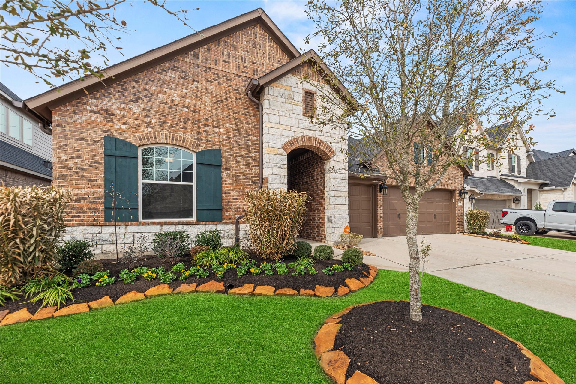 3127 Swift Way, Katy, TX 77493 Charming brick and stone exterior with lush landscaping and a welcoming arched entryway, complemented by a spacious driveway leading to a three-car garage.