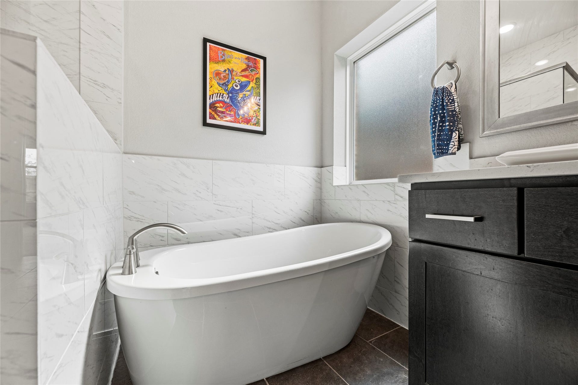 3127 Swift Way, Katy, TX 77493 Luxurious primary bathroom featuring a sleek freestanding tub, modern fixtures, and elegant tilework, complemented by a large frosted window for natural light and privacy.