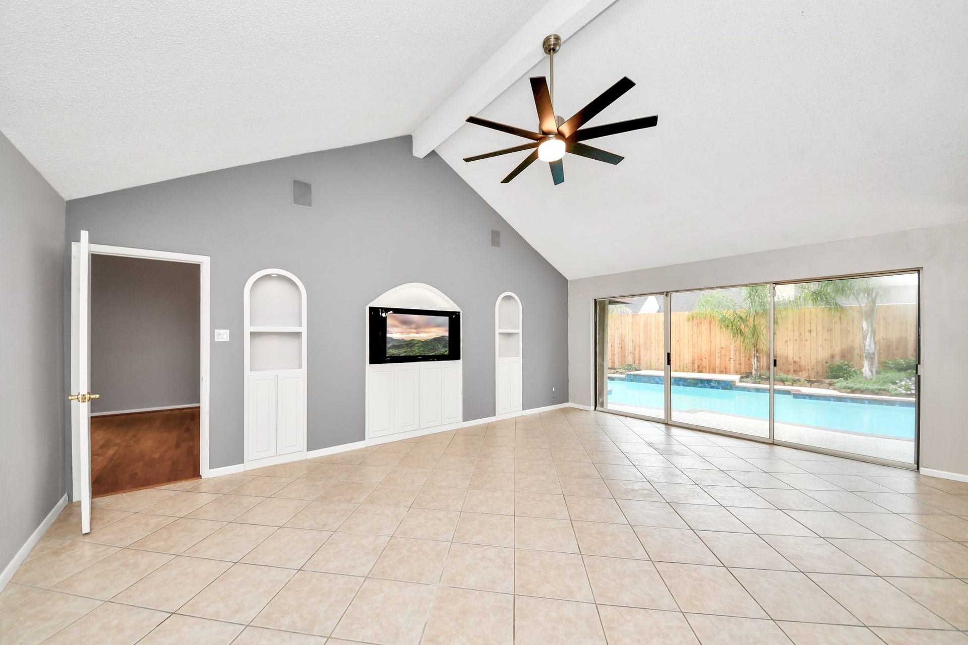 Unstaged view showcases the vaulted ceiling, updated fan, built-in cabinetry and expansive sliding glass doors overlooking the pool.