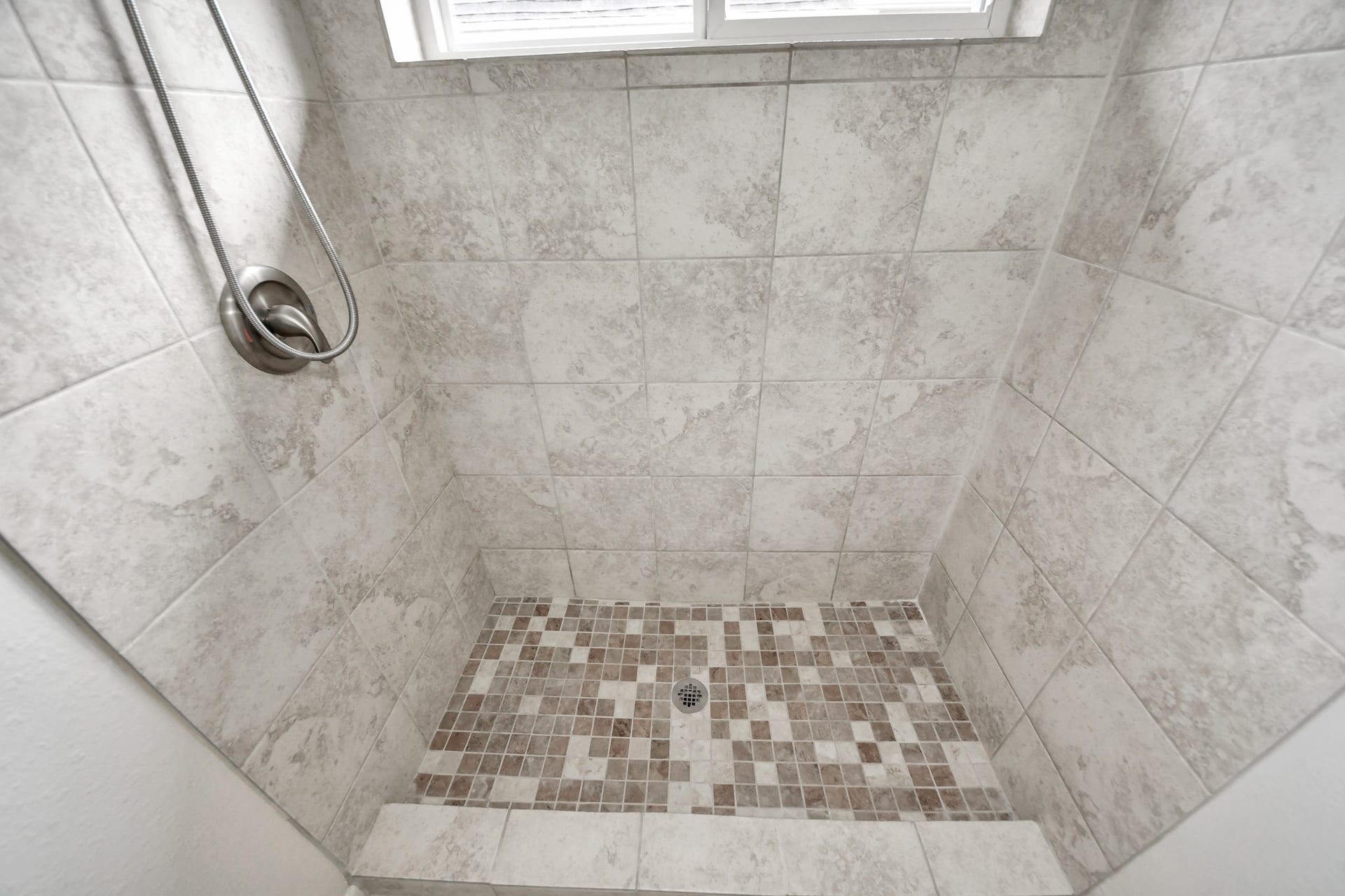 Detailed view of the tiled walk-in shower with decorative mosaic tile floor.