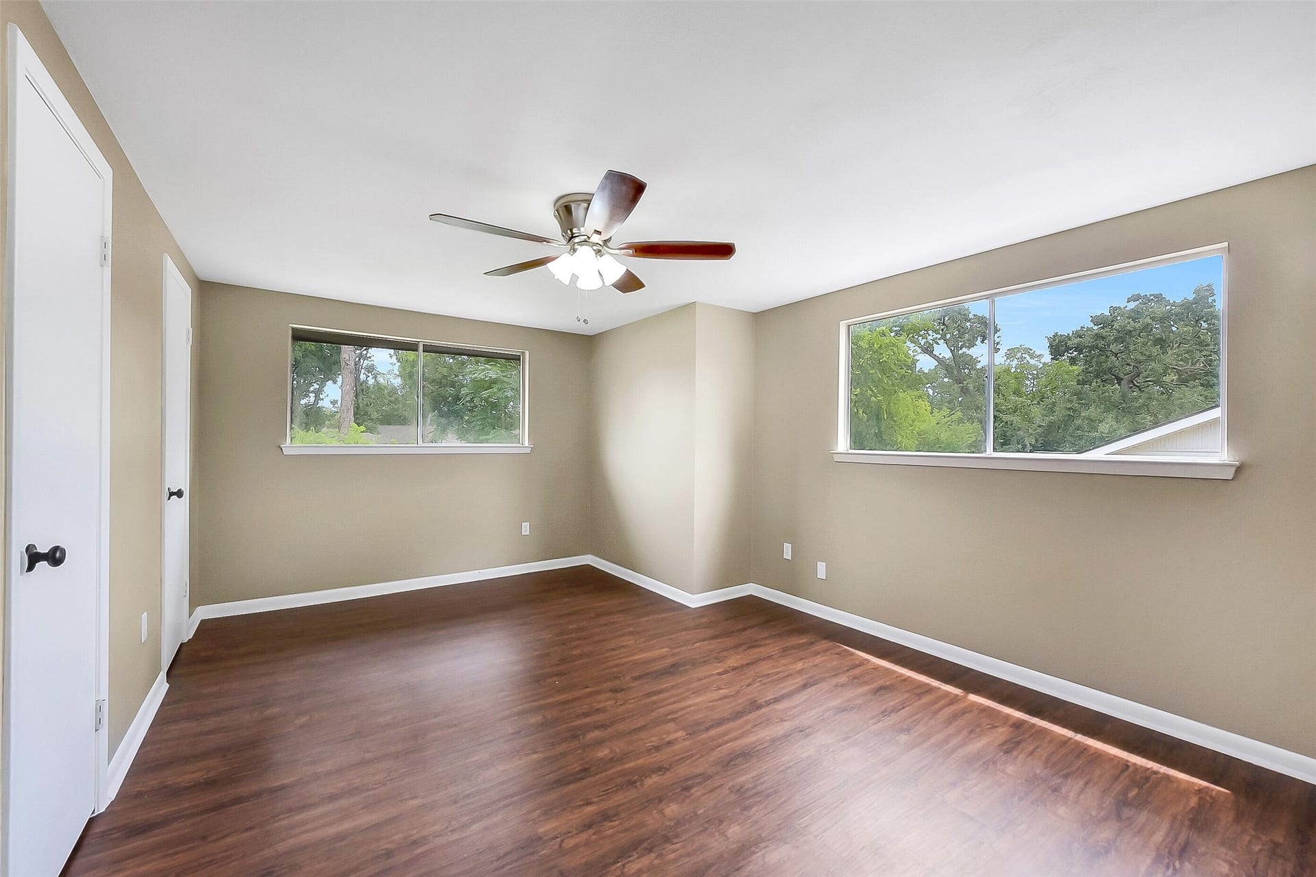 15503 Wandering Trail, Friendswood, TX 77546 This upstairs bedroom features large windows for abundant natural light, wood-look flooring, dual closets, and a ceiling fan, creating a bright and versatile space.