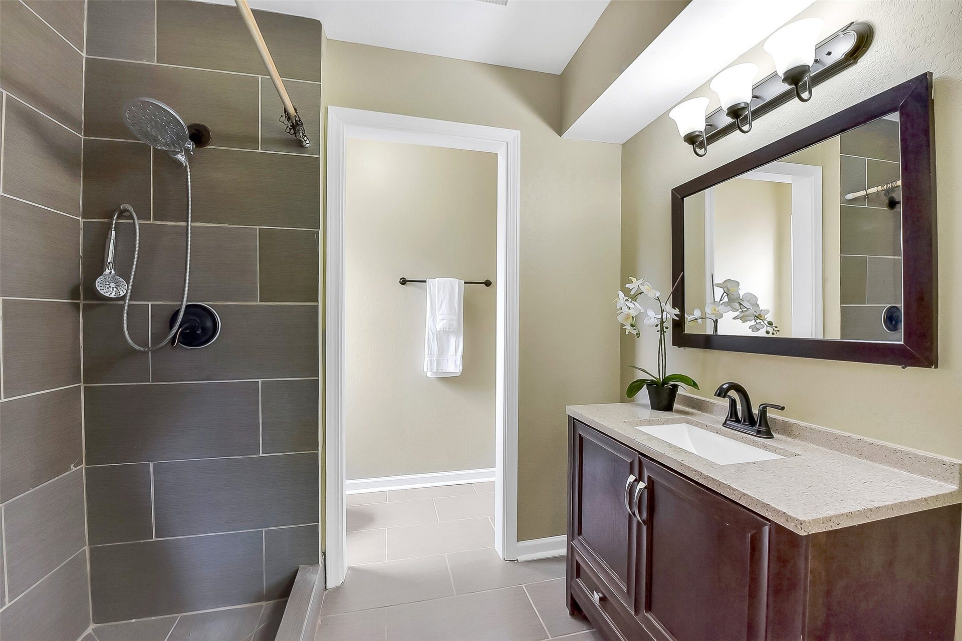 15503 Wandering Trail, Friendswood, TX 77546 The master bathroom features a modern design with a sleek vanity topped with a solid-surface countertop, framed mirror, and updated lighting. The spacious walk-in shower is accented with oversized tile, a built-in bench, a grab bar, and dual showerheads, including a rain-style fixture.