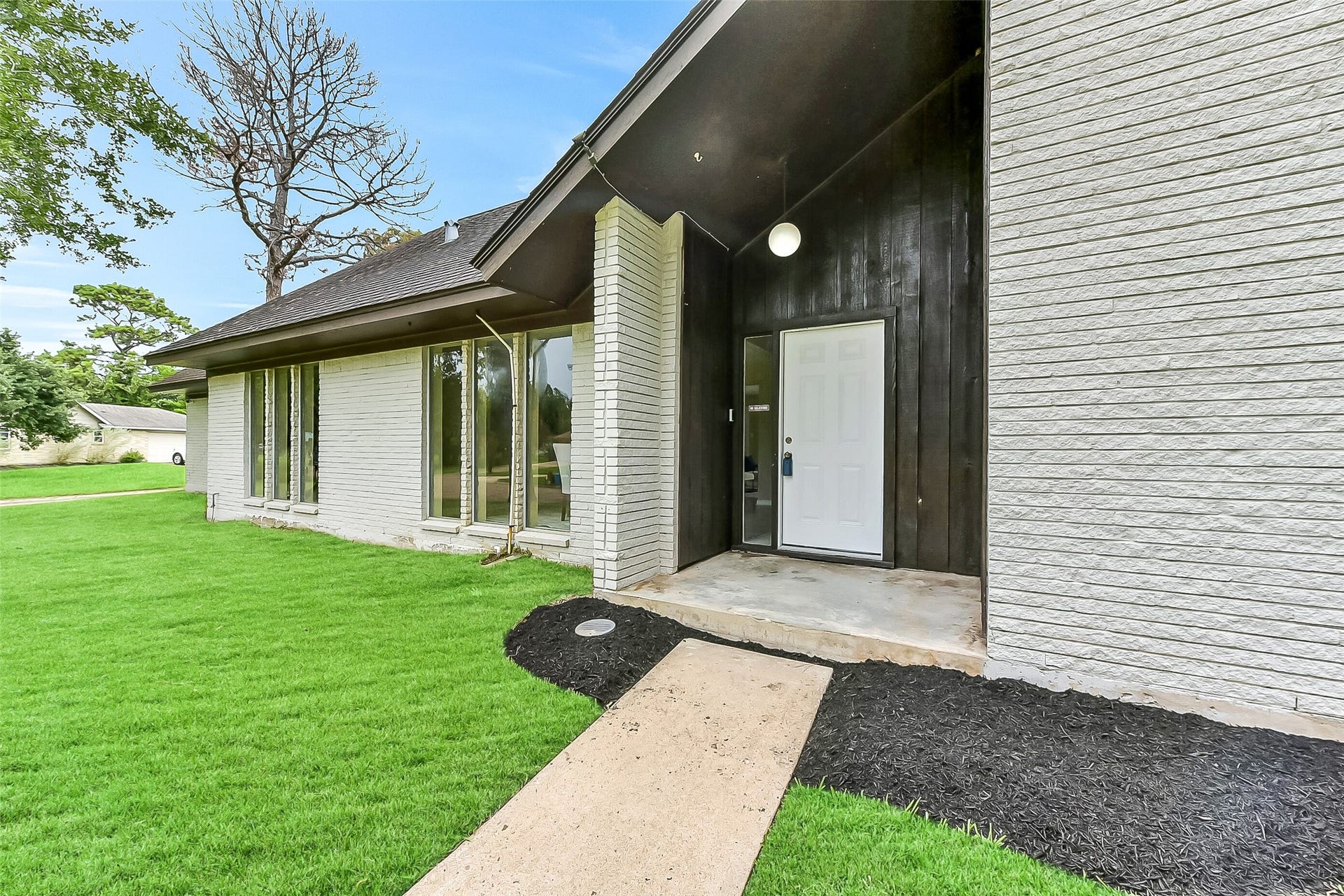 15503 Wandering Trail, Friendswood, TX 77546 A welcoming covered front entry framed by tall windows sets the tone for this 3,019-square-foot home, showcasing fresh exterior updates and a modern contrast of painted brick and dark wood accents.