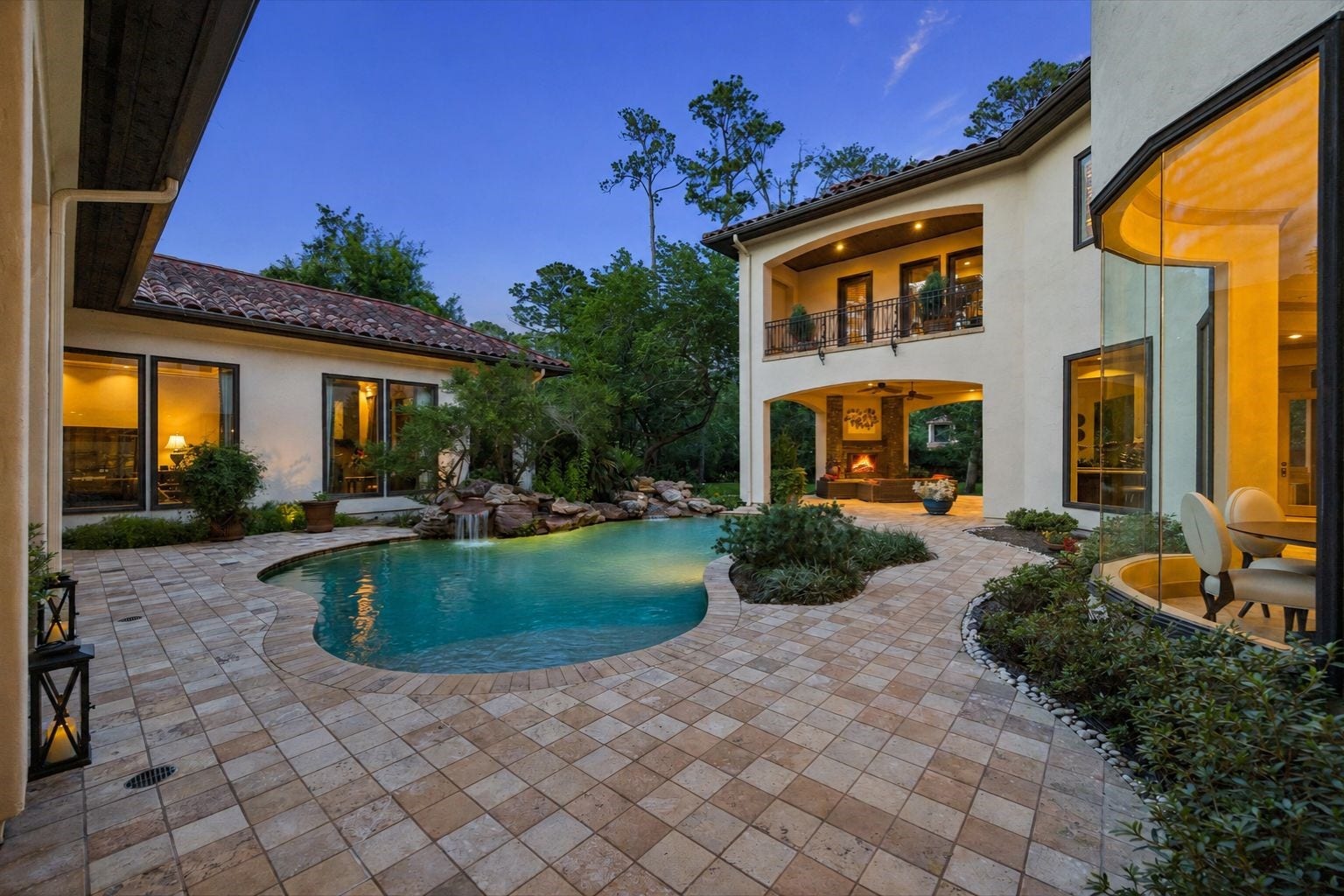 2 Lacewood Lane, Piney Point Village, TX 77024 Evening courtyard view showcasing the resort-style pool, waterfall feature, covered outdoor living, and warm interior glow.